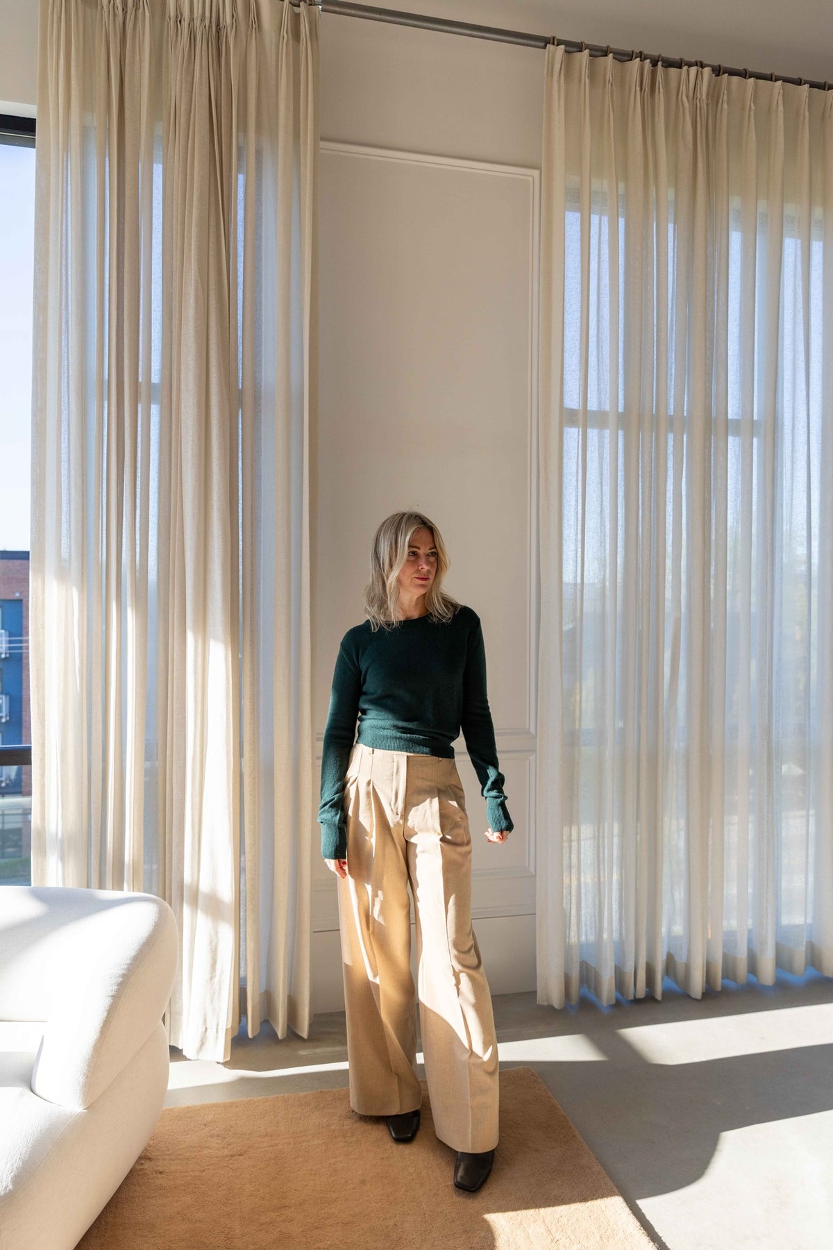 by Malene Birger Cymbaria Pants in sand with a dark green Eterne sweater, full-length view in a sunlit loft