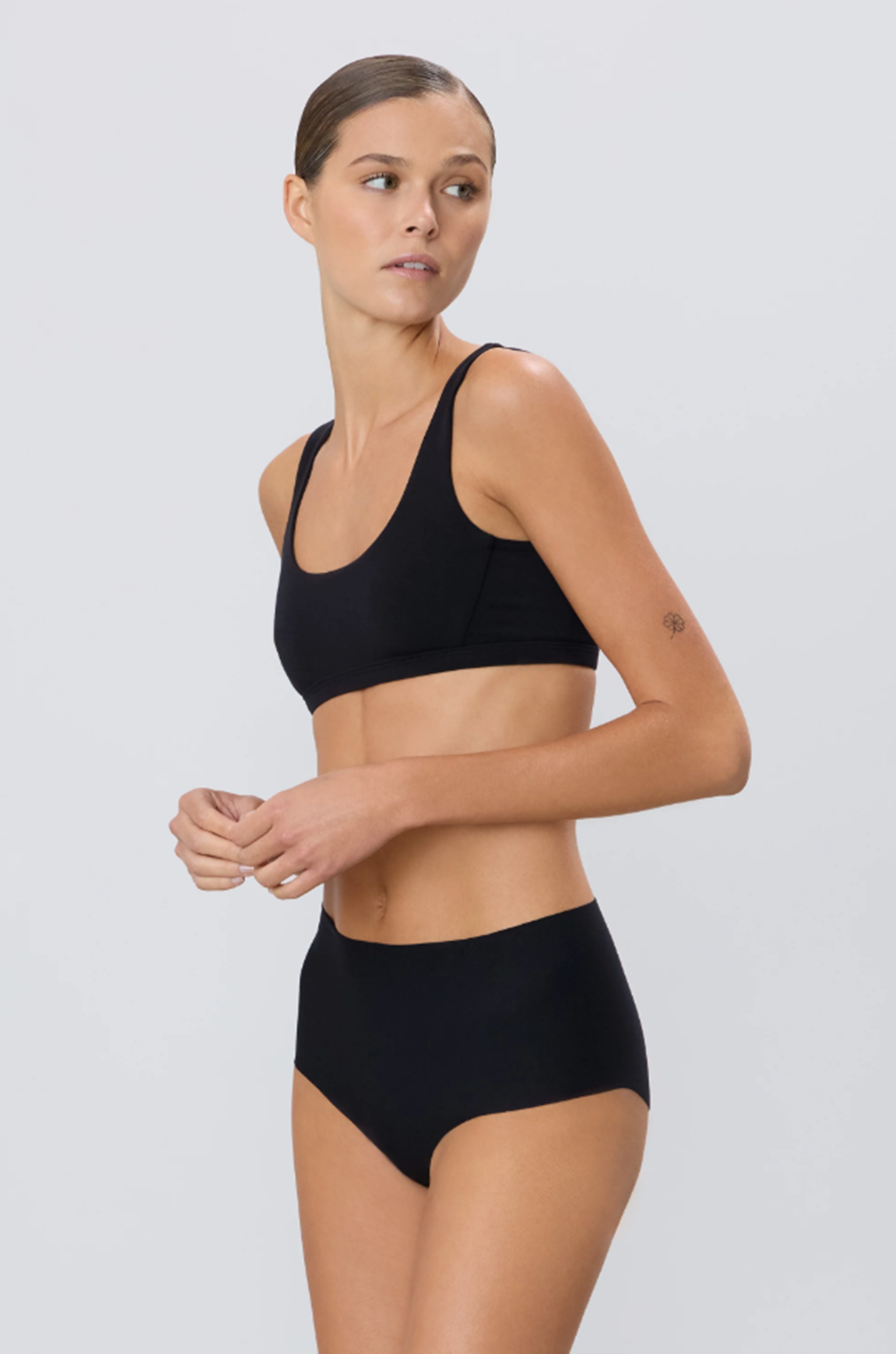 Woman wearing a black sports bra and high-waisted underwear on a light gray background