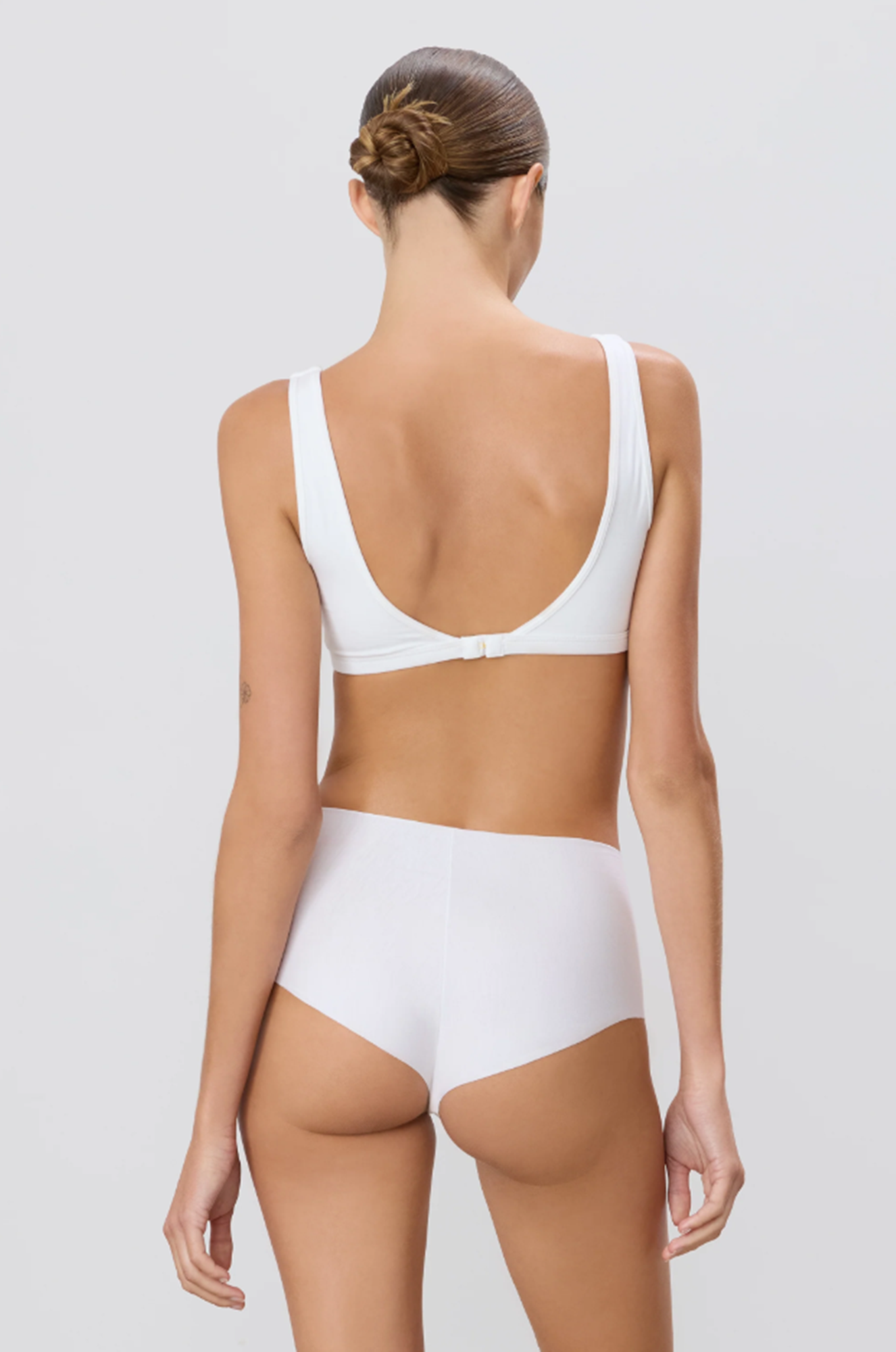back of a oman wearing an ivory sports bra and underwear set on a plain background