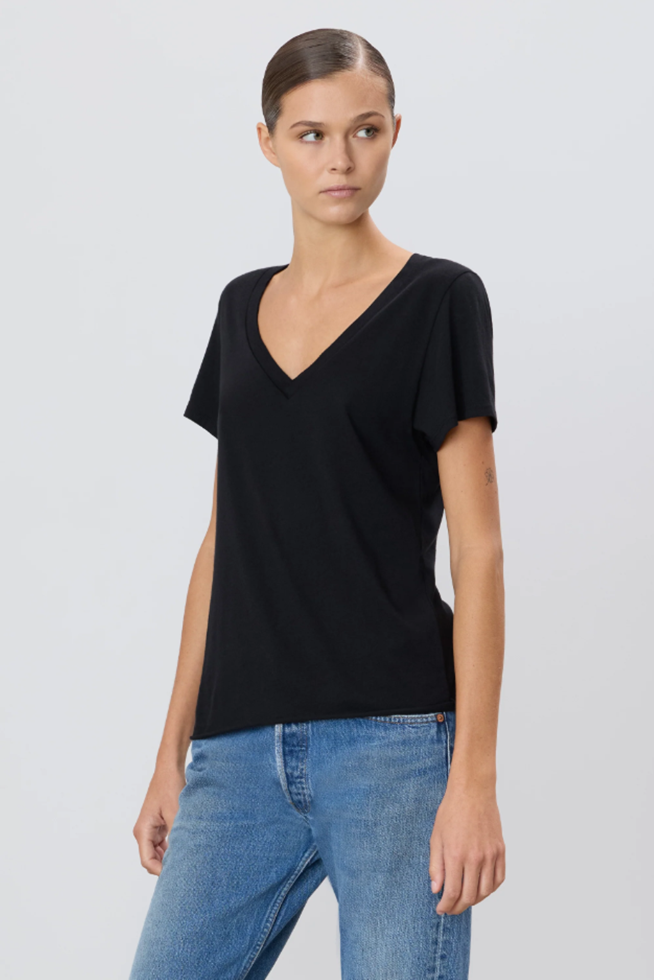 Woman wearing a black V-neck t-shirt and blue jeans on a light gray background