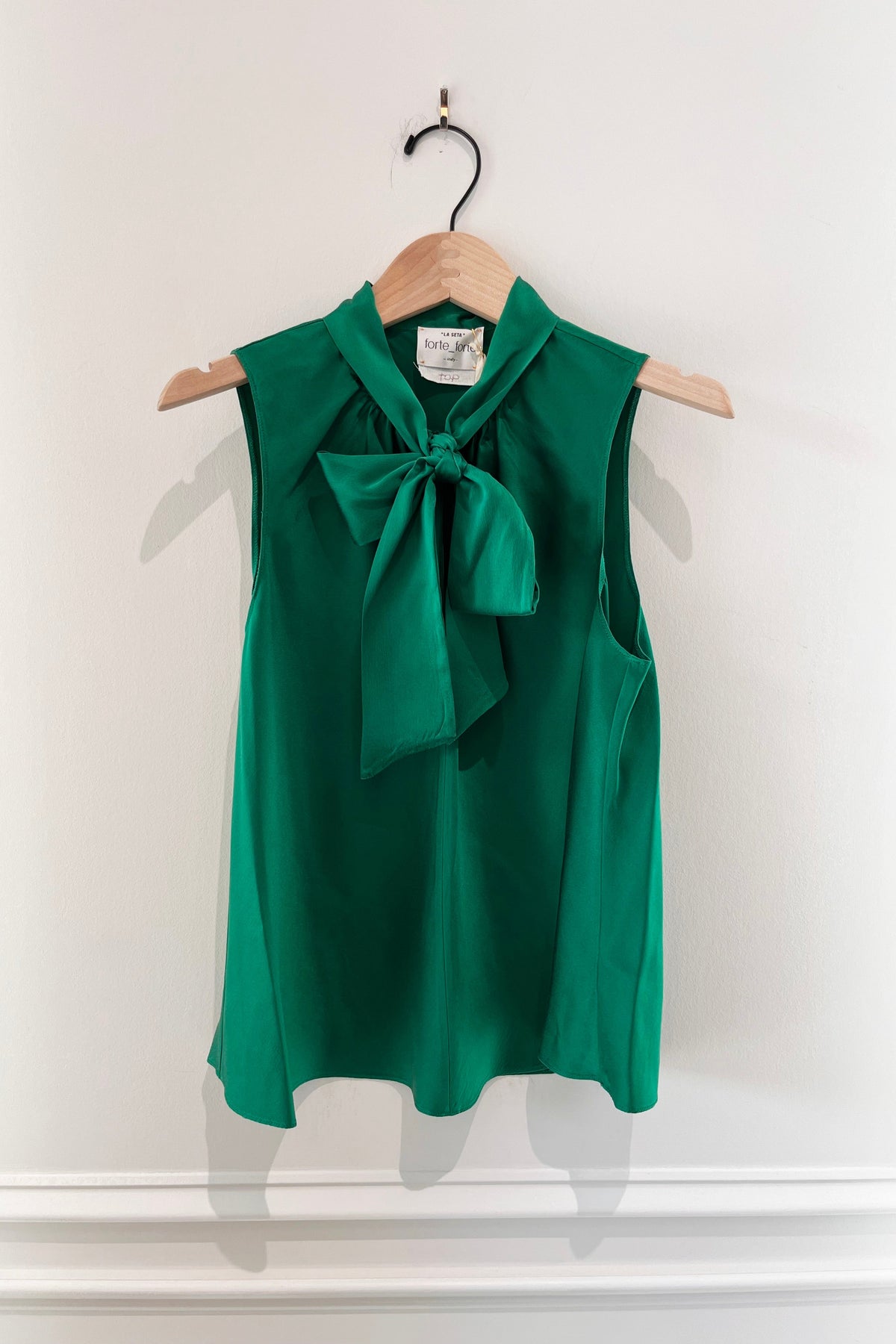 Forte Forte Silk Satin Lavalliere Top in Royal, a sleeveless emerald green silk satin blouse with a pussy-bow tie neckline on a hanger