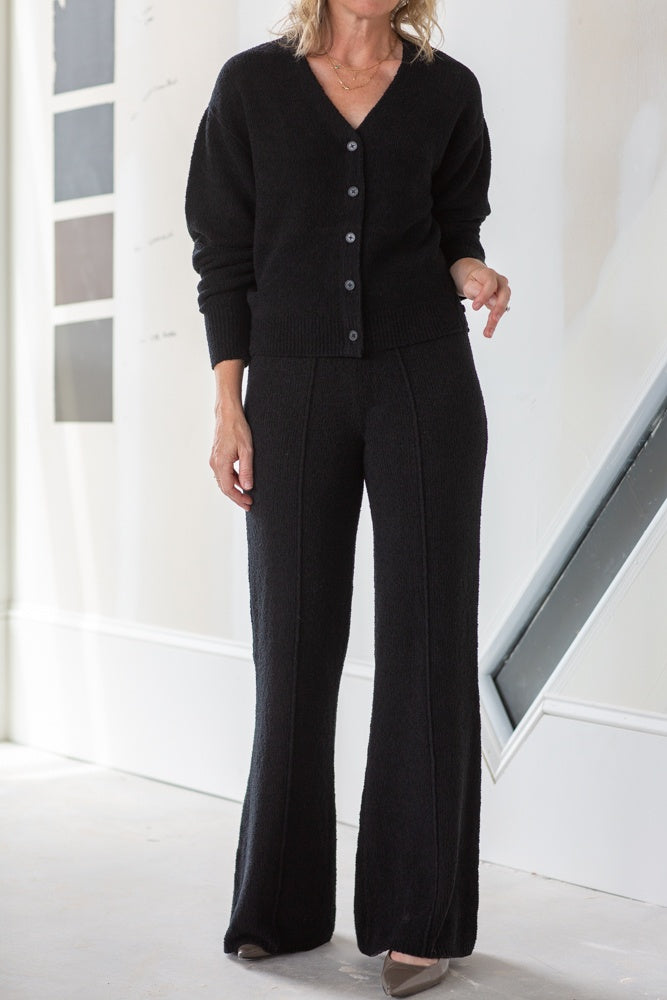 Woman wearing a black cardigan and pants in a minimal indoor setting
