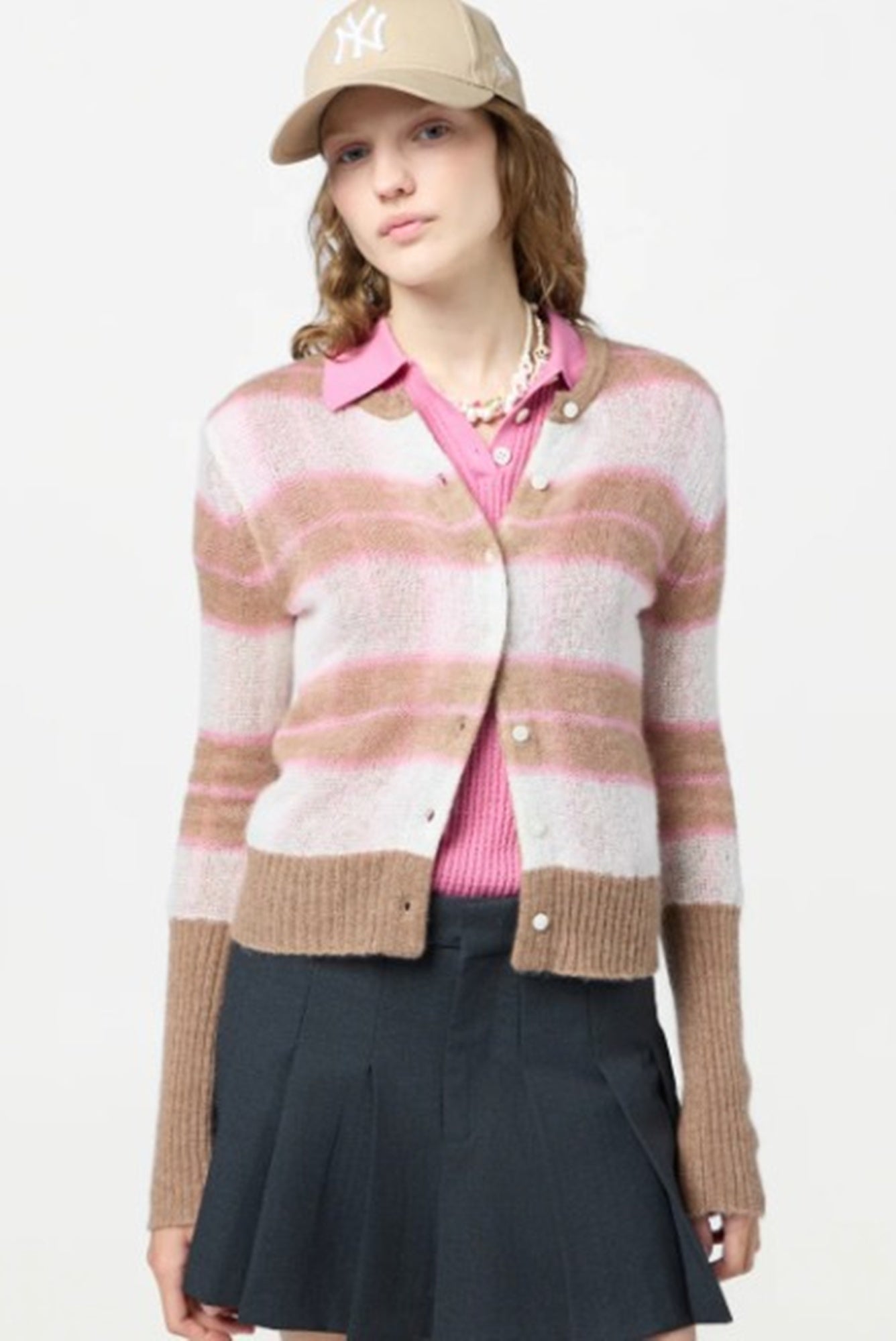 Woman wearing a striped cardigan, pink shirt, and navy skirt on a white background