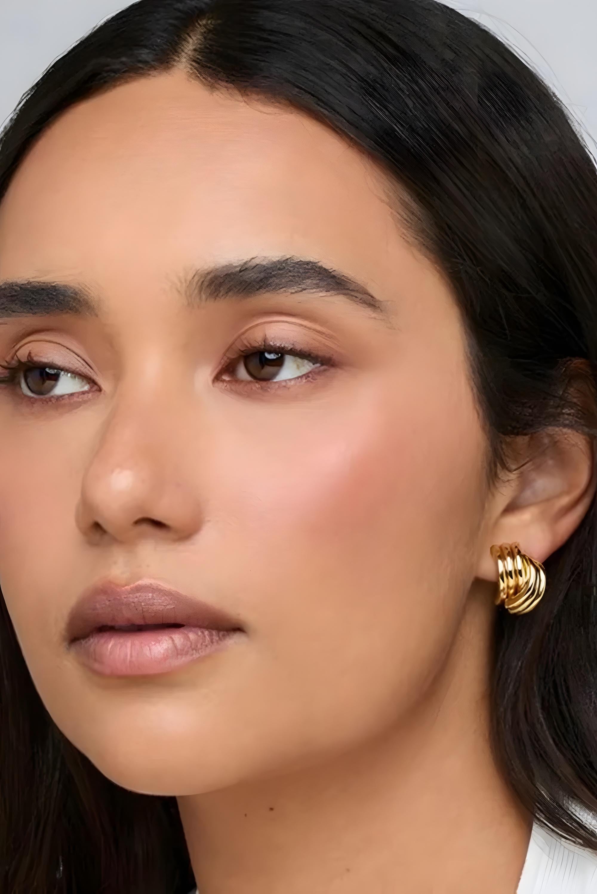 Close-up of a woman wearing gold hoop earrings with a neutral background