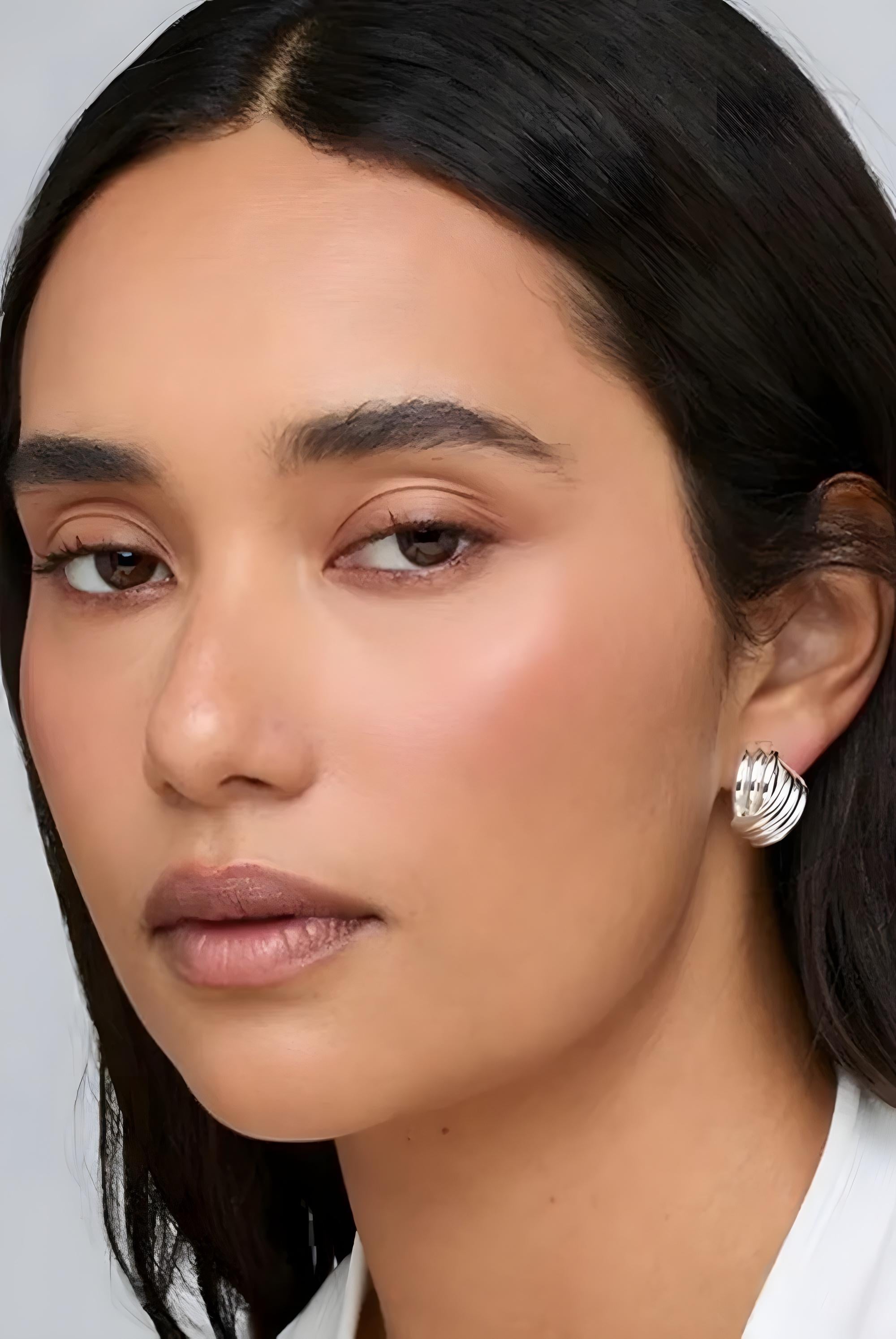 Close-up of a woman wearing silver hoop earrings against a neutral background