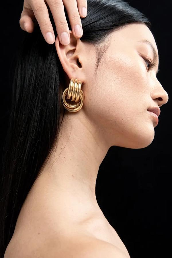 Close-up of a person wearing gold hoop earrings with a hand adjusting the earring.