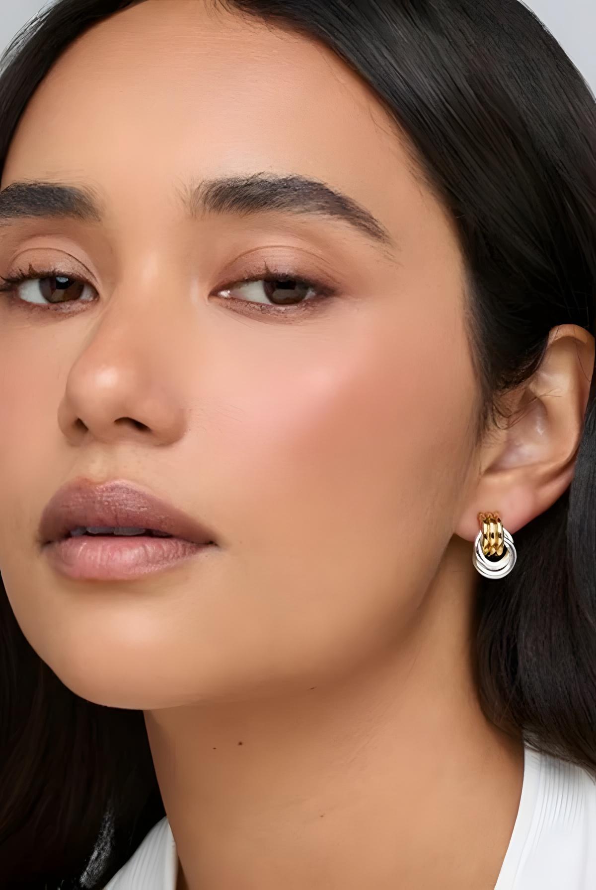 Close-up of a woman wearing gold hoop earrings with a neutral background