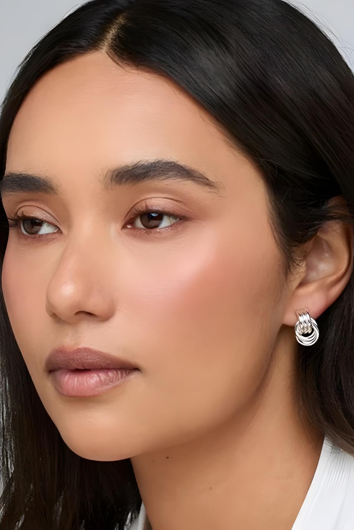 Close-up of a person wearing a silver hoop earring with a white background