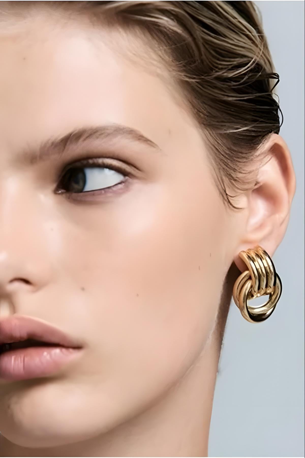 Close-up of a woman wearing gold hoop earrings against a neutral background