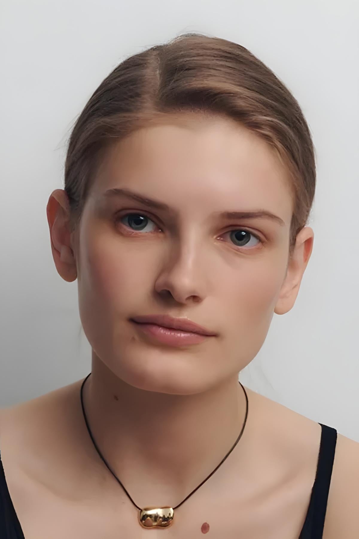Woman wearing a necklace with a gold pendant against a plain background