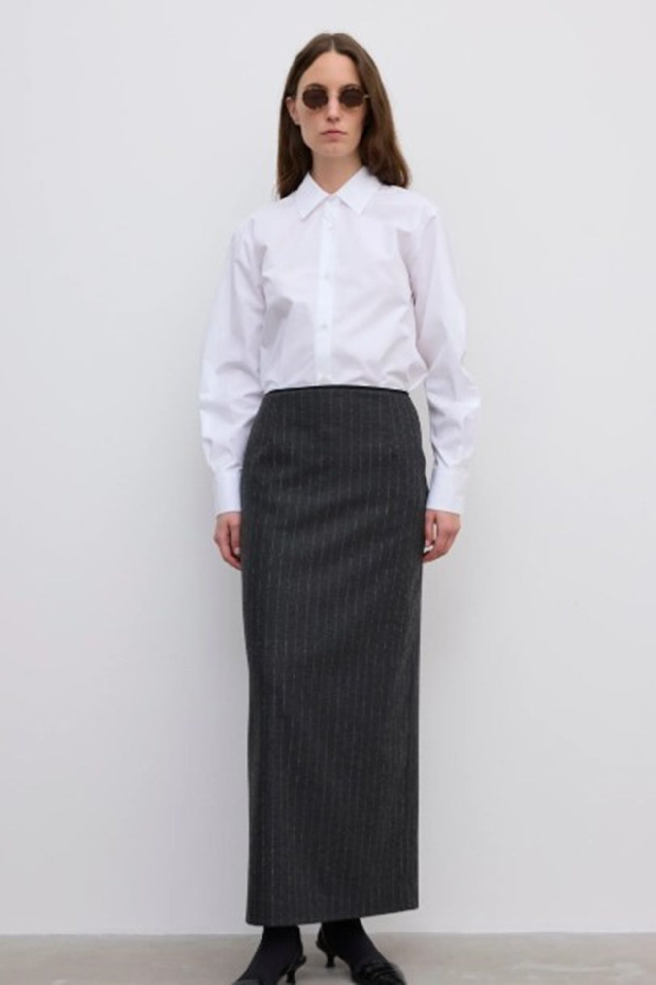 Woman wearing a white shirt and long black skirt against a plain background