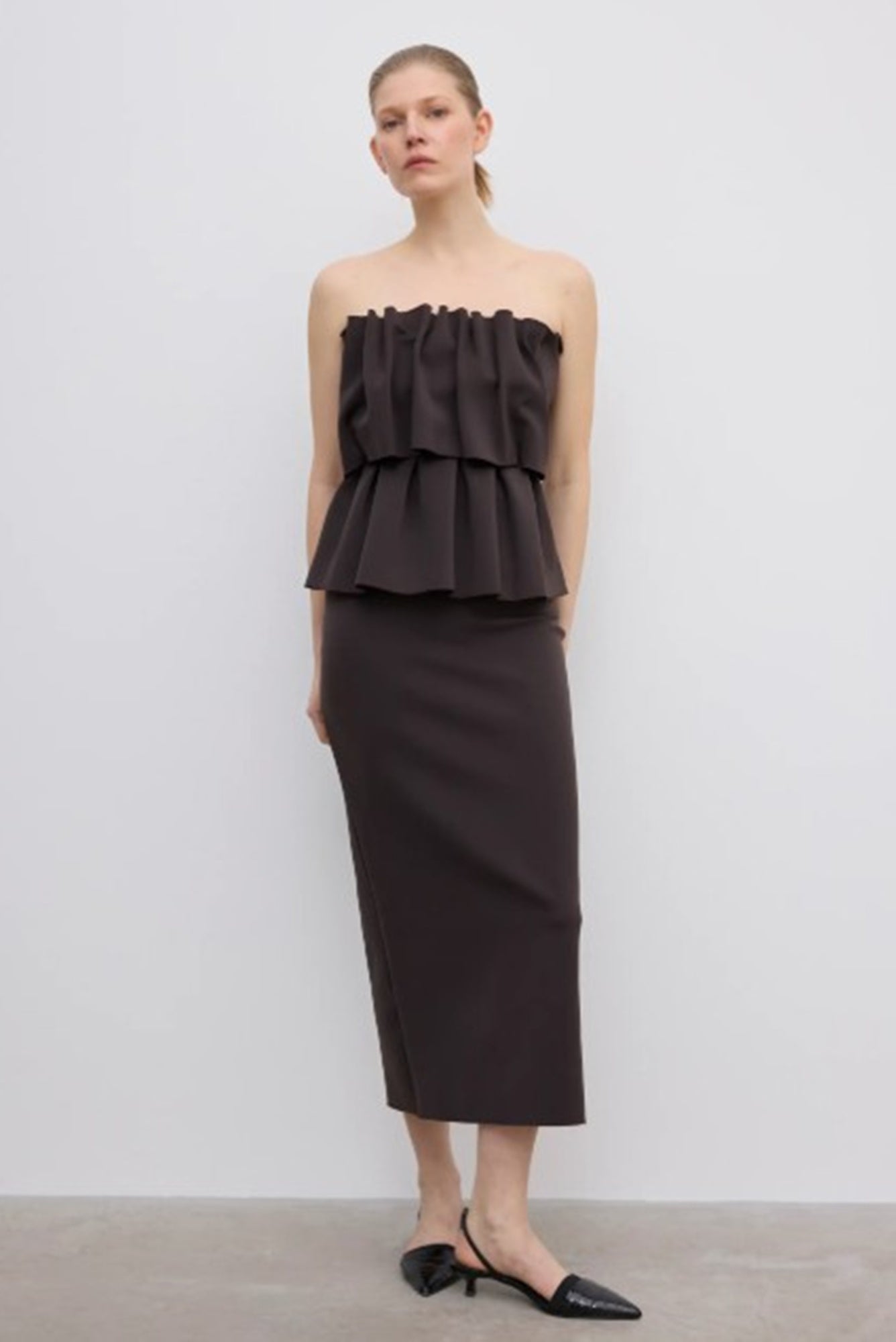 Woman wearing a dark brown strapless top and pencil skirt on a light gray background