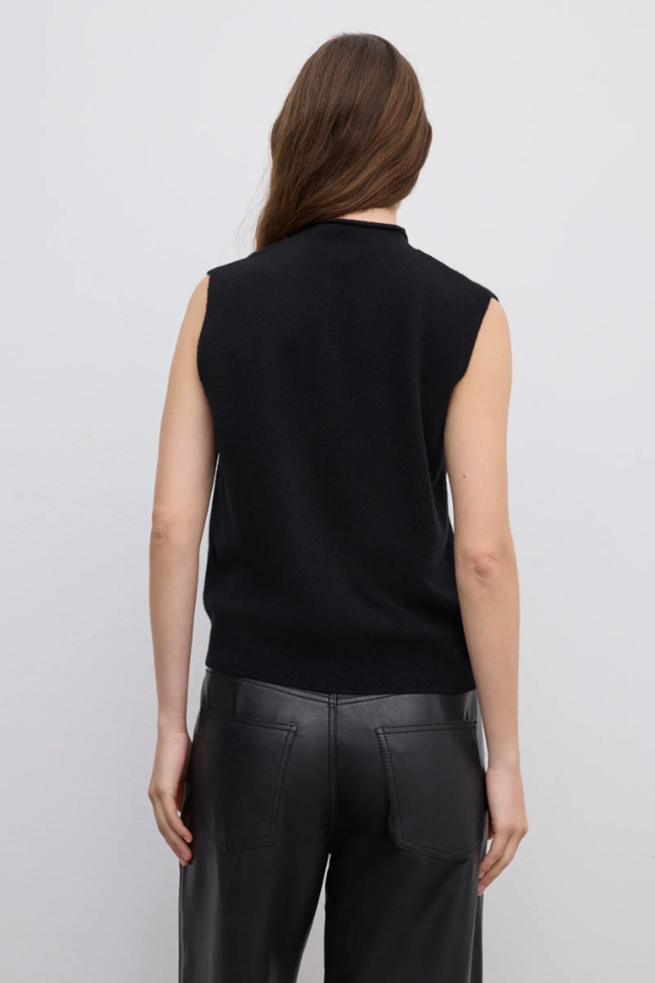 Back of a Person wearing a black sleeveless cashmere sweater and black pants against a light gray background