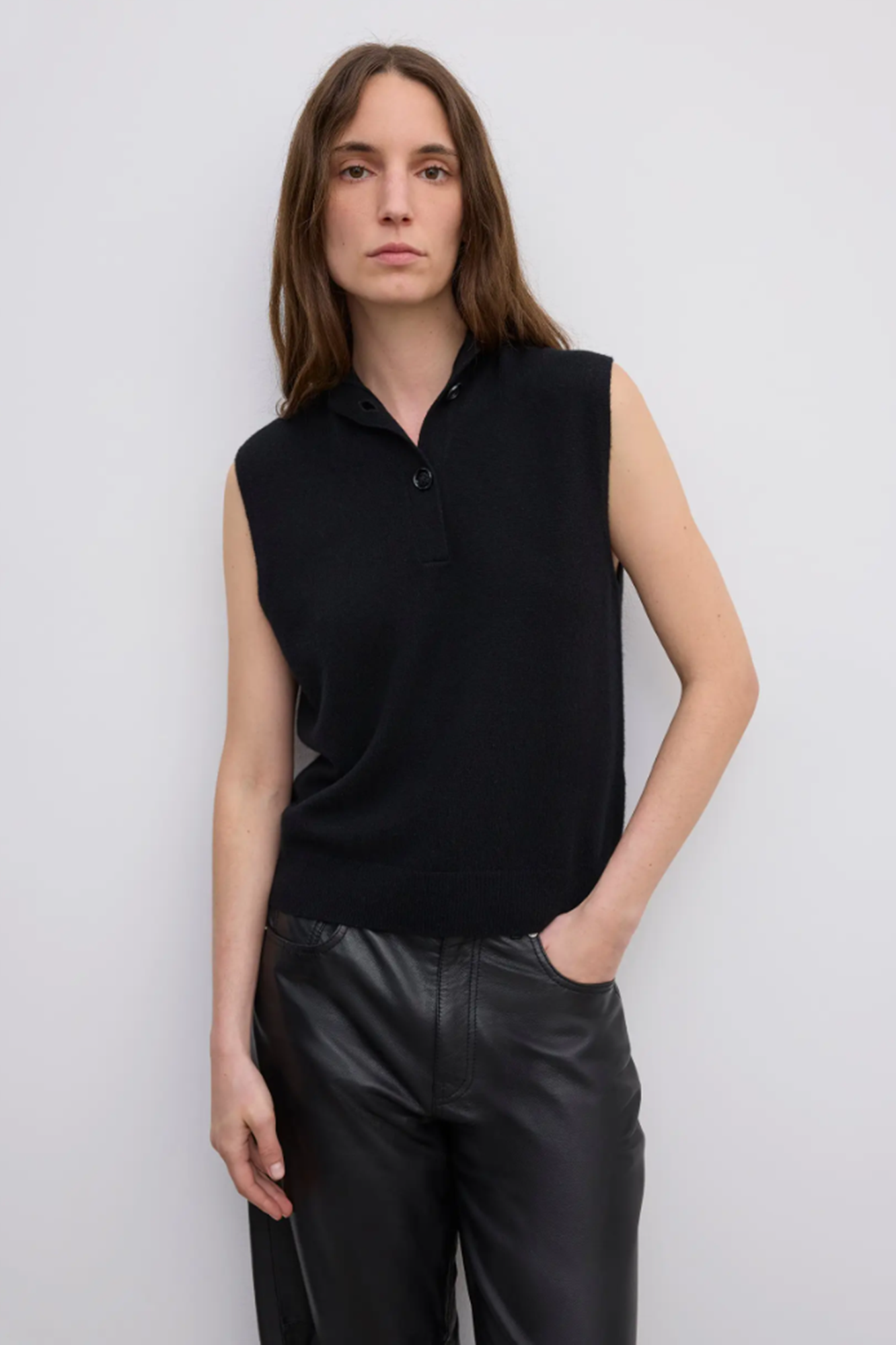 Person wearing a black sleeveless cashmere sweater and black pants against a white background