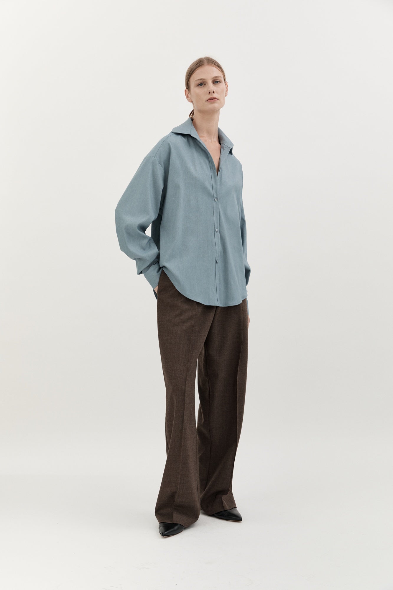 Person wearing a light blue shirt and brown pants on a white background