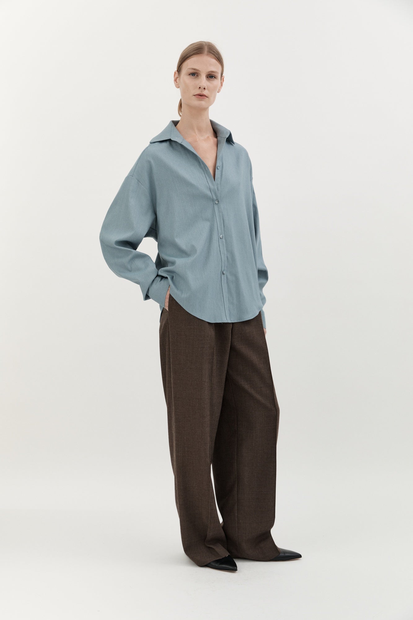 Person wearing a light blue shirt and brown pants on a white background