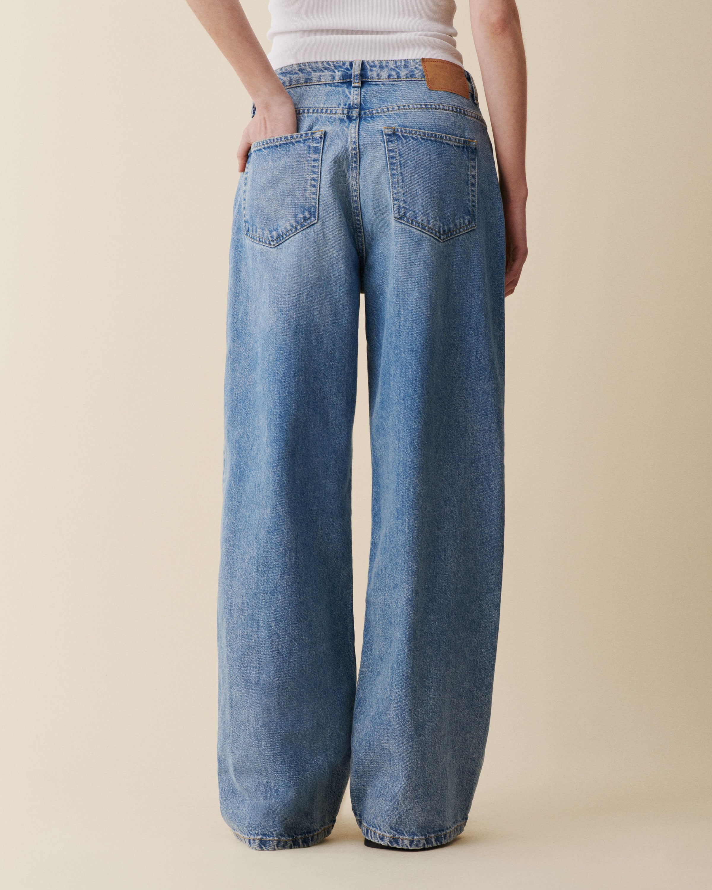 Person wearing blue wide-leg jeans on a beige background