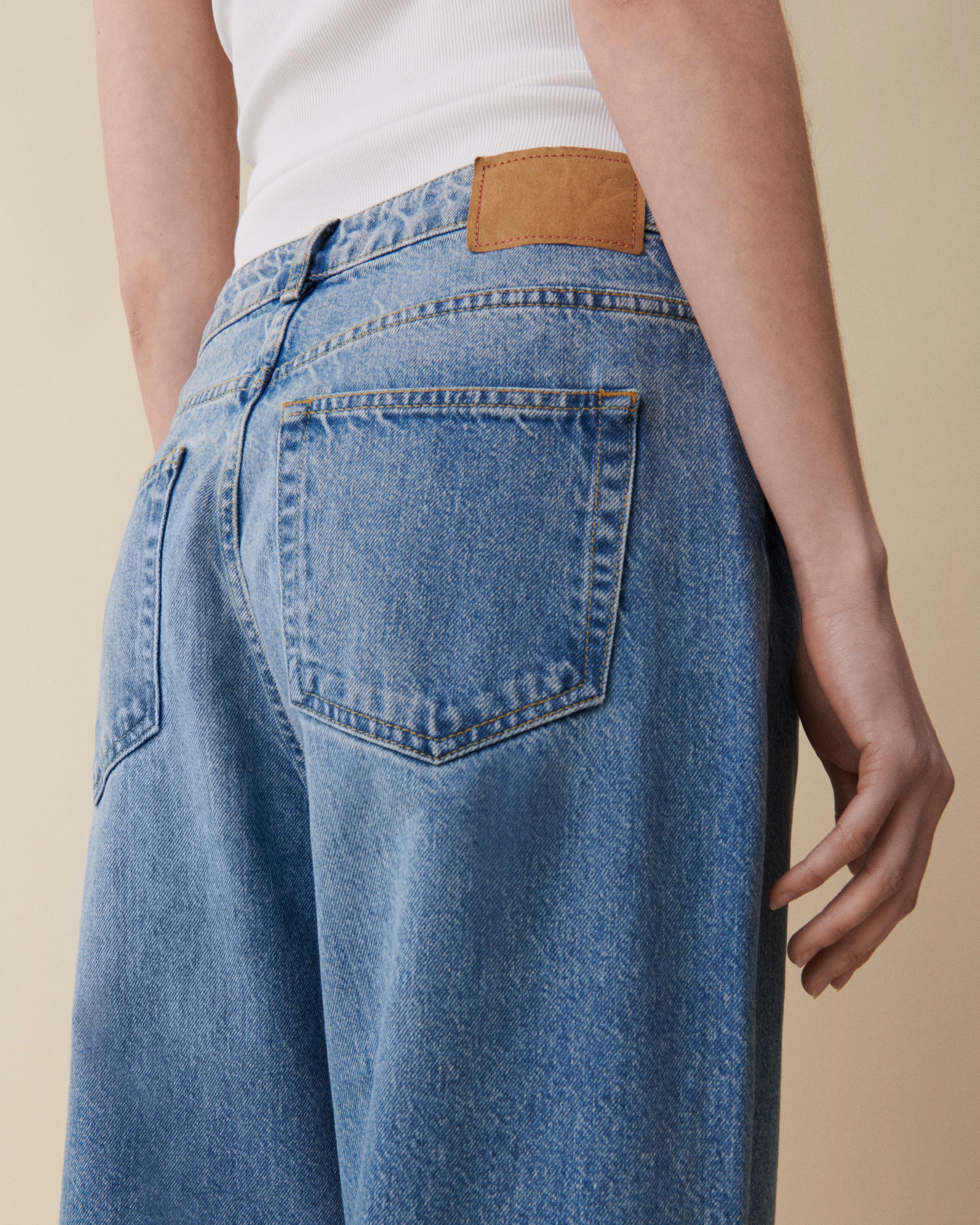 Person wearing blue jeans with a beige patch on a neutral background
