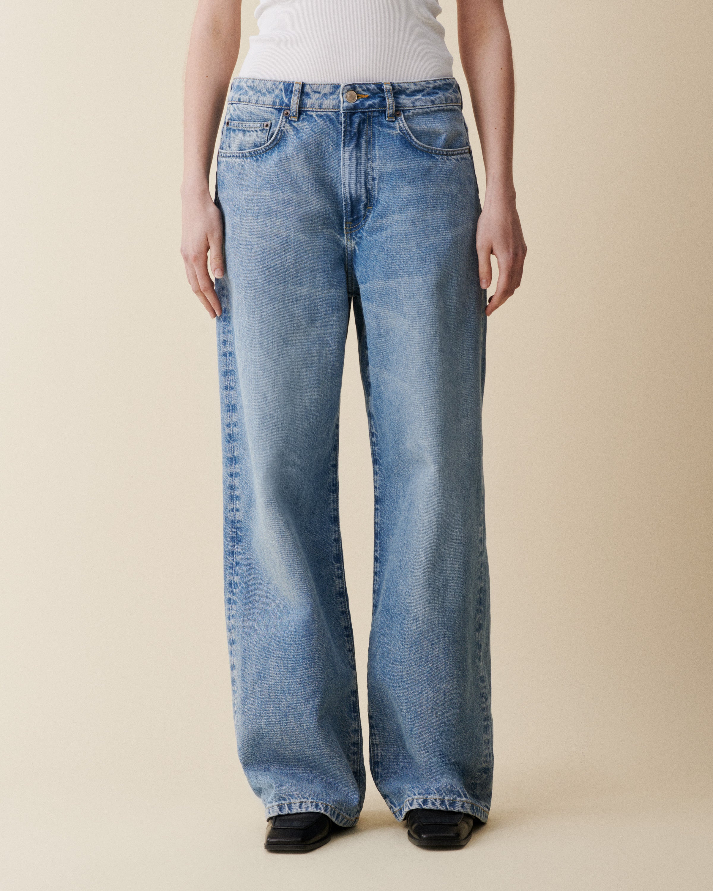 Person wearing light blue jeans on a beige background