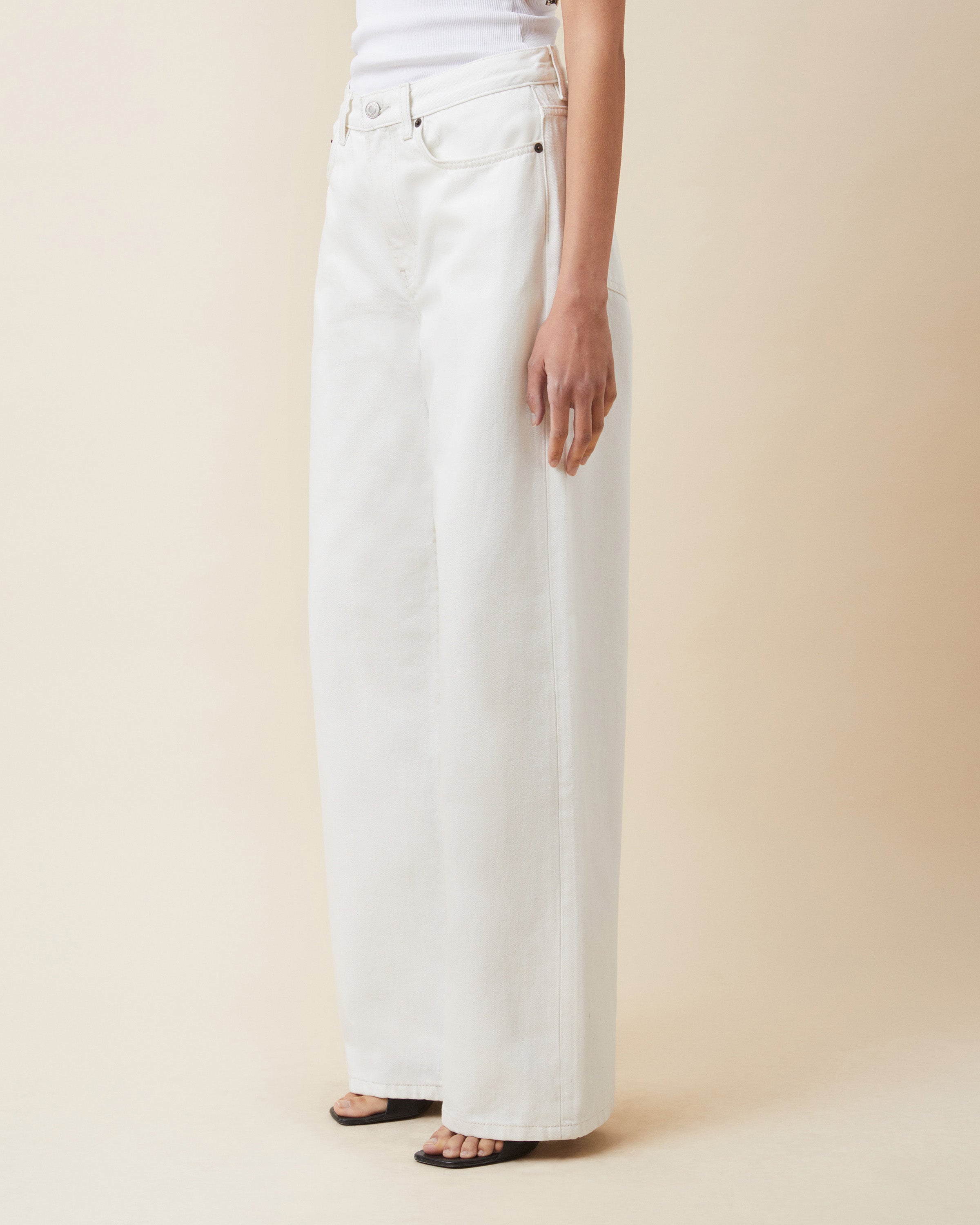 Person wearing white wide-leg jeans on a beige background