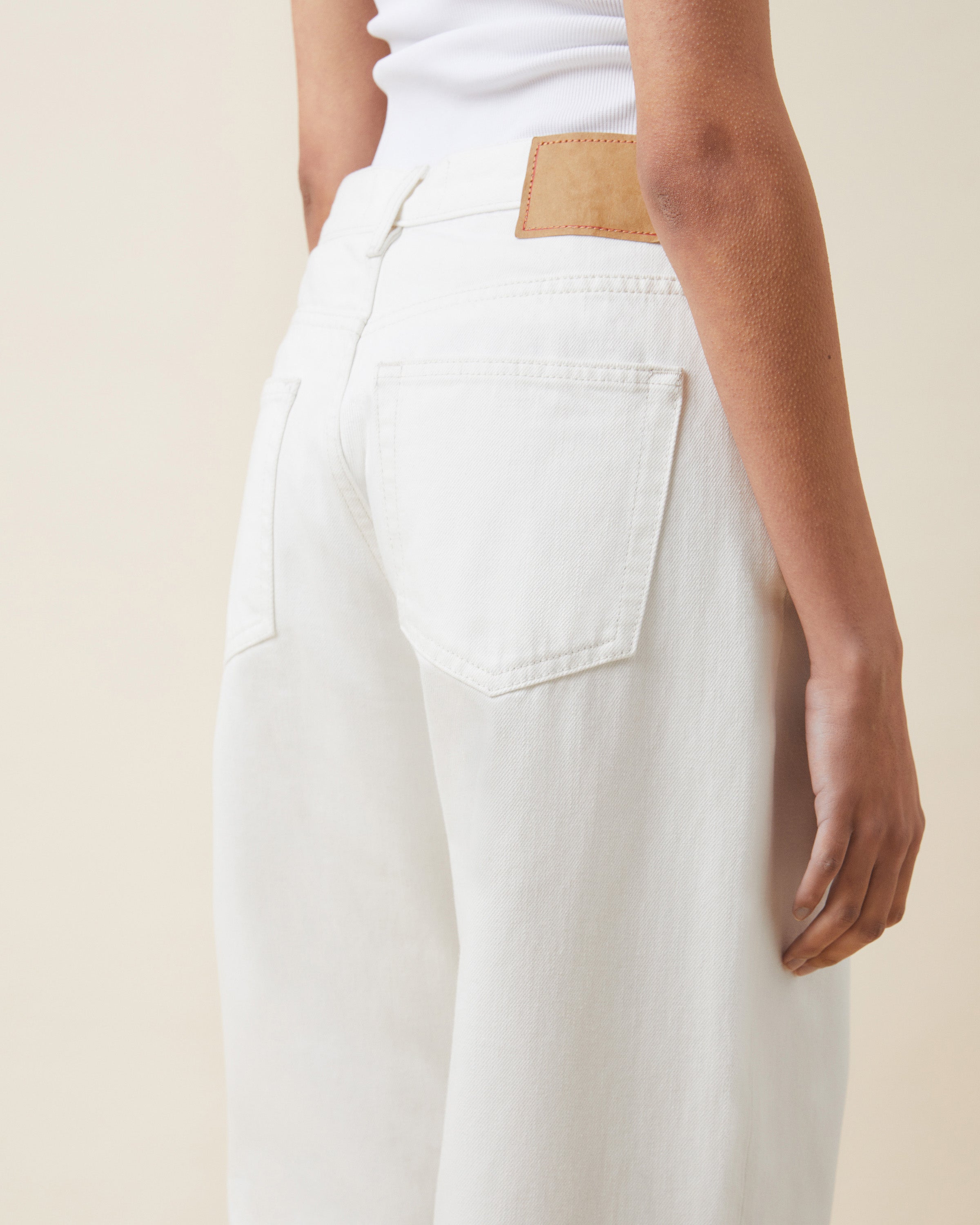 Person wearing white pants with a beige belt on a plain background
