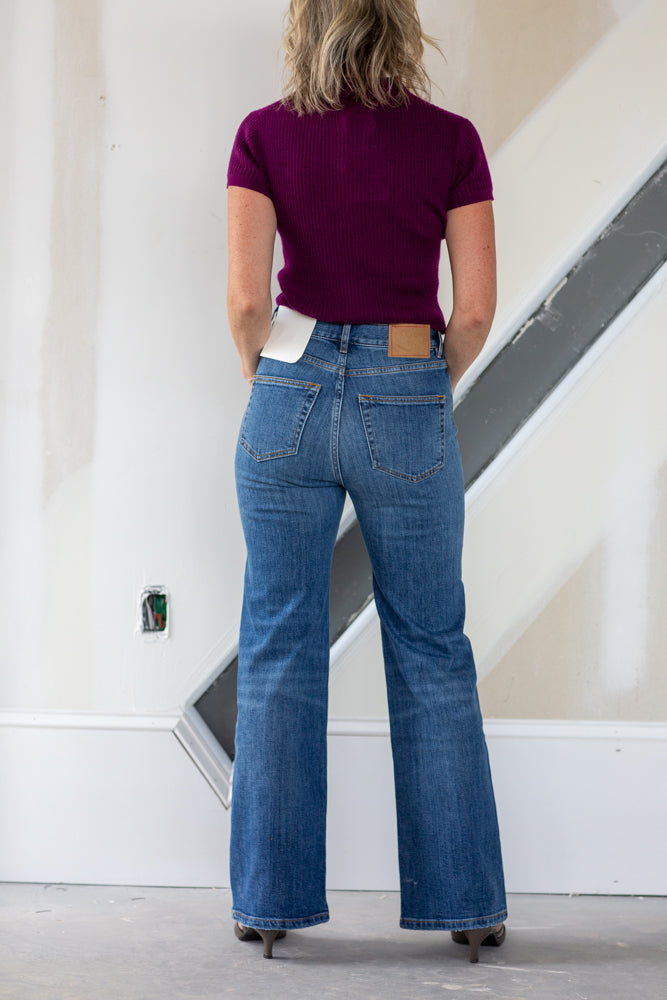 Person wearing blue jeans and a purple top standing in a room with white walls and a staircase.