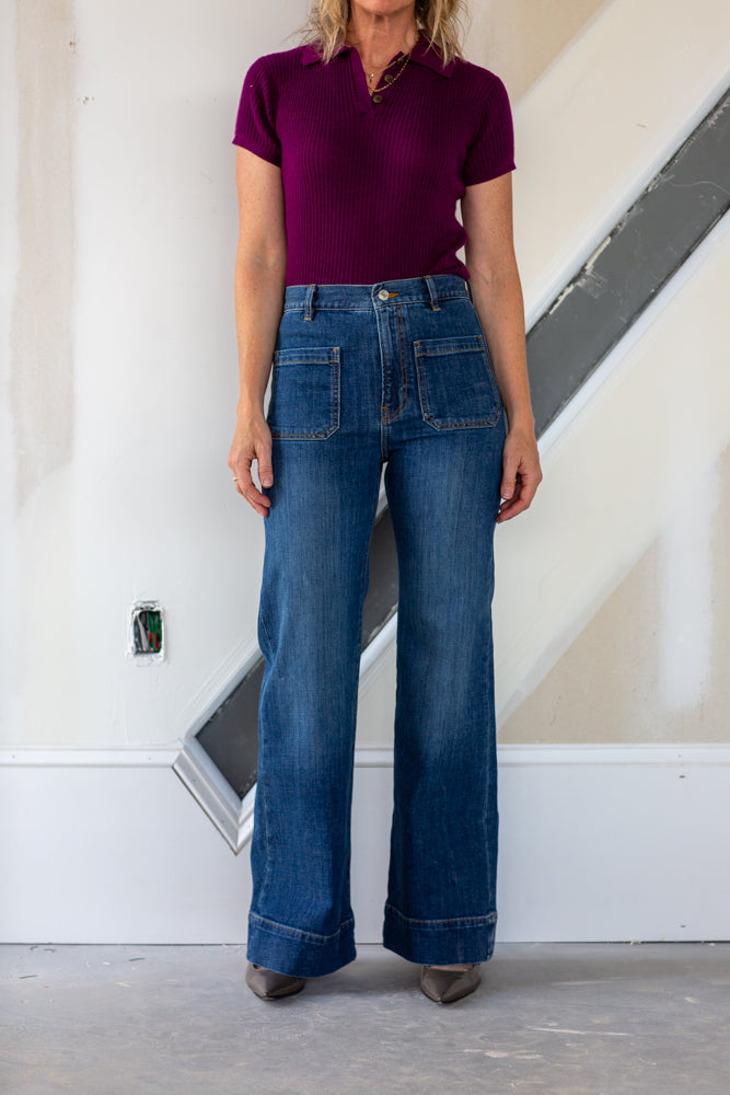 Person wearing a purple shirt and blue jeans standing indoors.