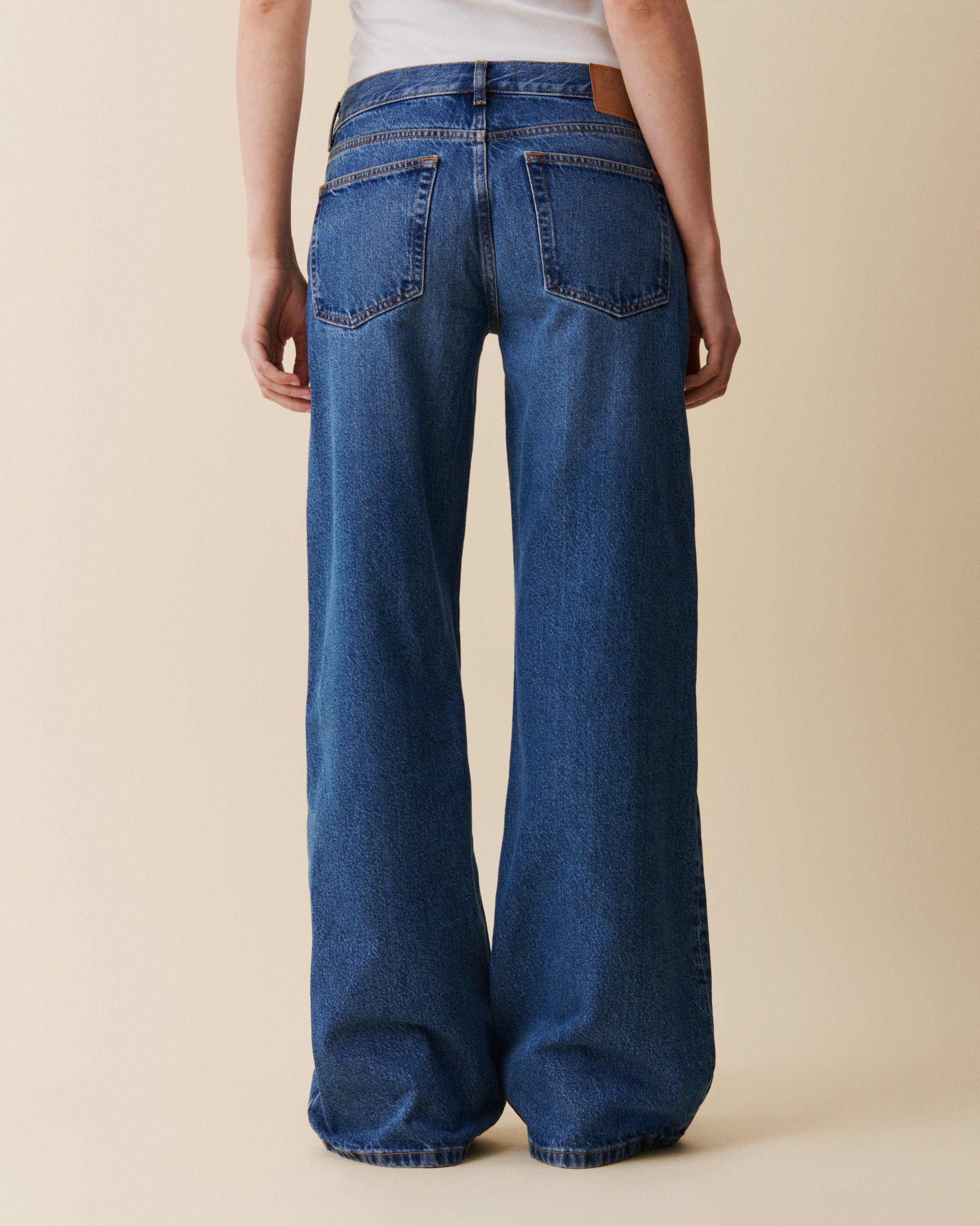Person wearing blue wide-leg jeans on a beige background