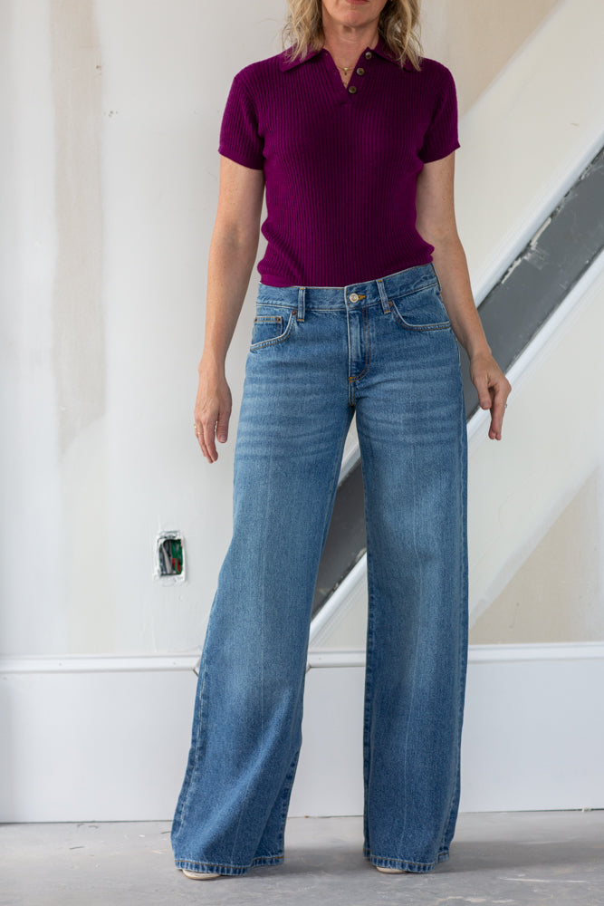 Person wearing a purple polo shirt and blue jeans standing indoors.