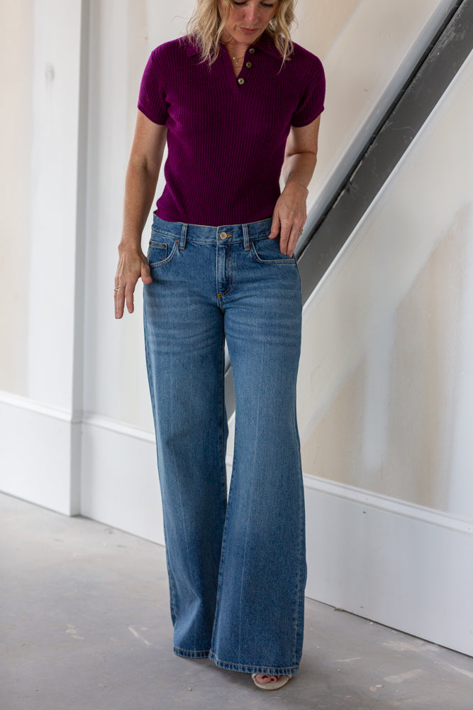 Woman wearing a purple shirt and blue jeans indoors.