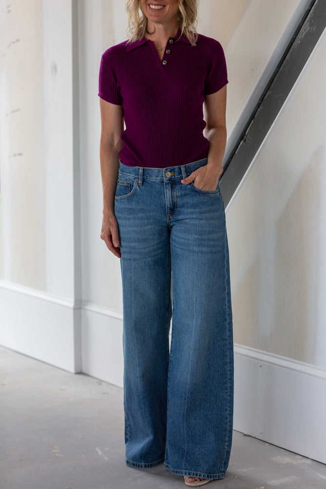 Person wearing a maroon polo shirt and blue jeans standing indoors.