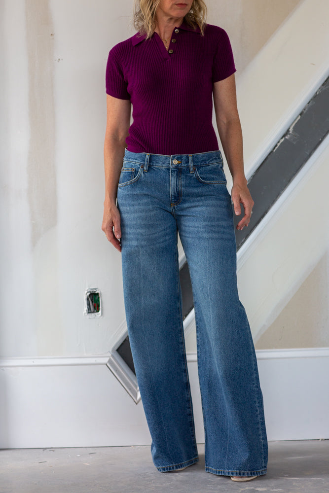 Person wearing a purple polo shirt and blue jeans standing indoors.