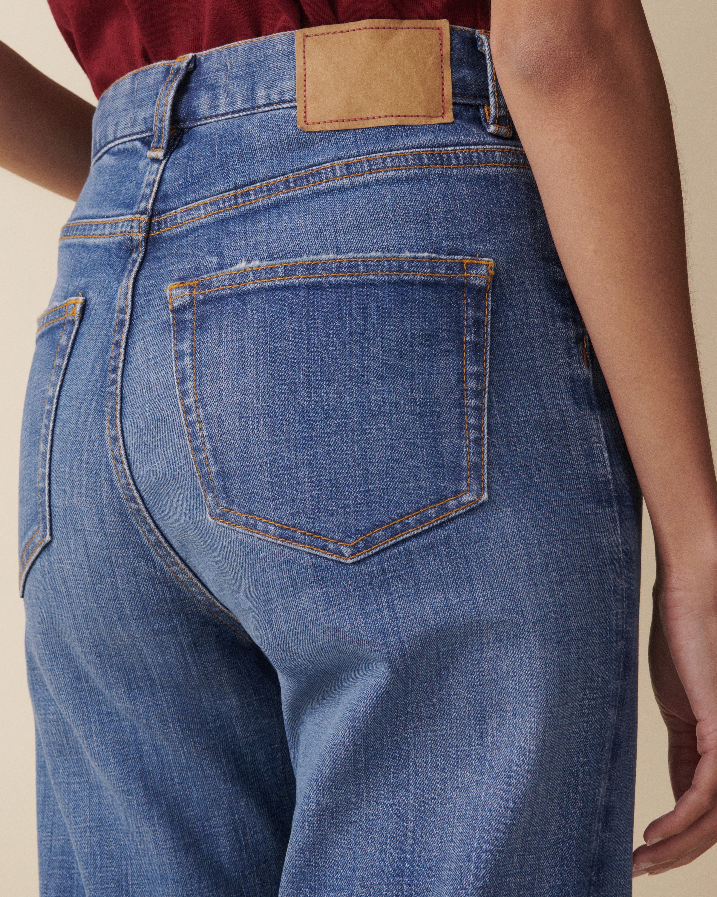 Close-up of blue jeans with a brown leather patch on a beige background