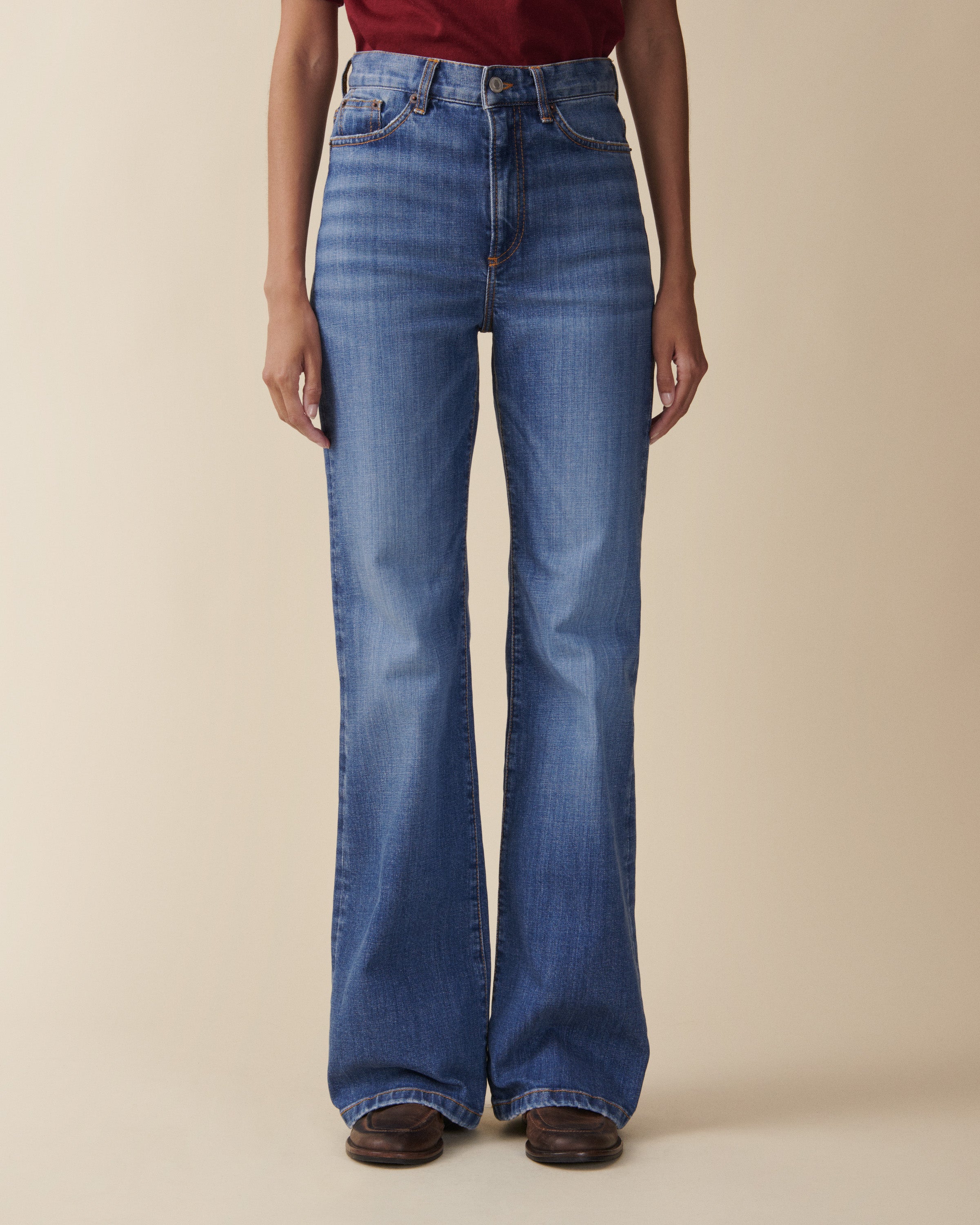 Person wearing blue flared jeans on a beige background