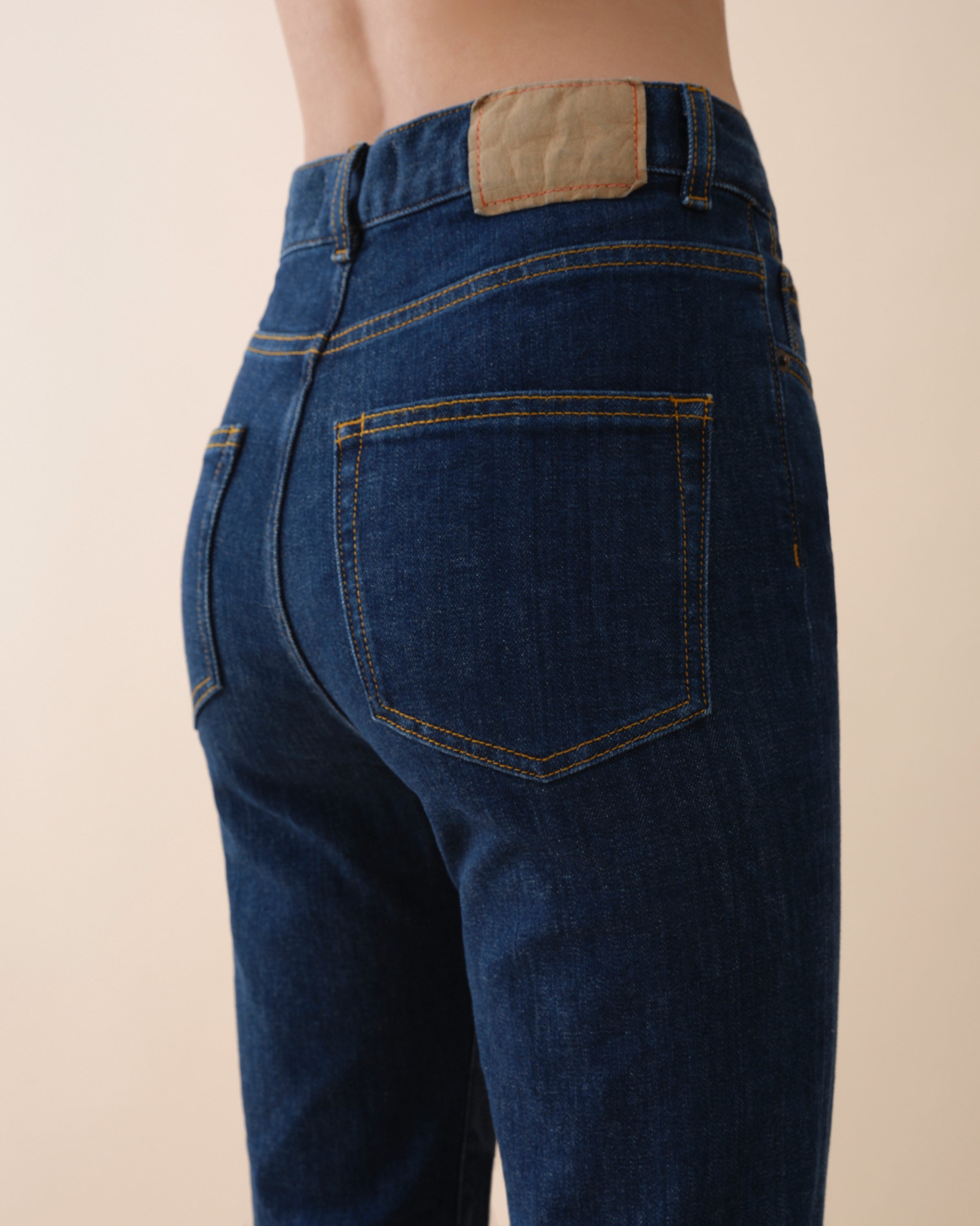 Blue jeans with a beige patch on the back pocket against a beige background