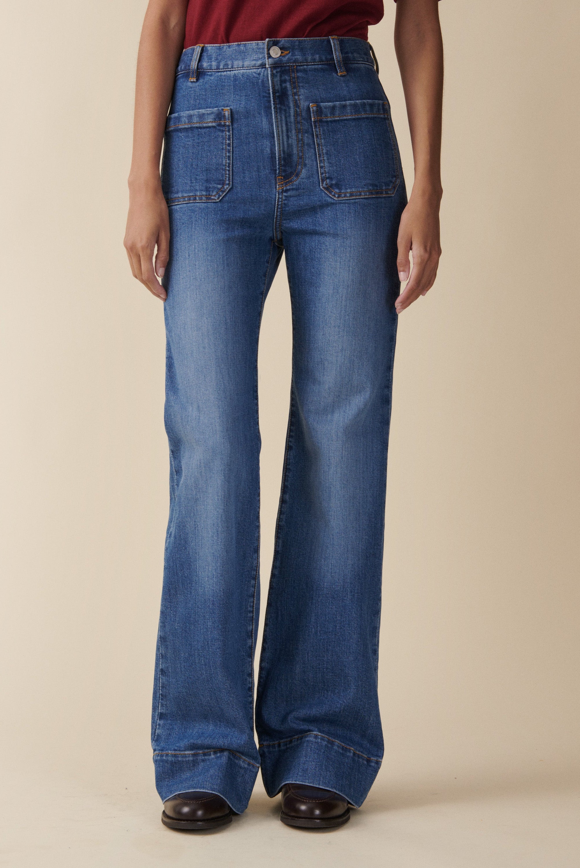 Person wearing blue flared jeans on a beige background