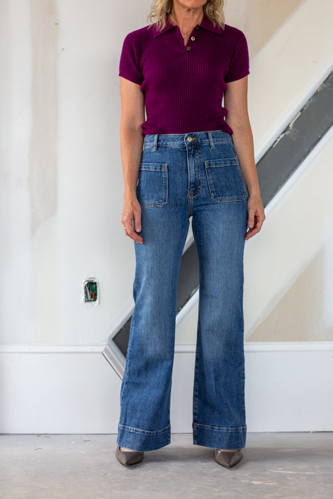 Person wearing a purple shirt and blue jeans standing in a room with a staircase.