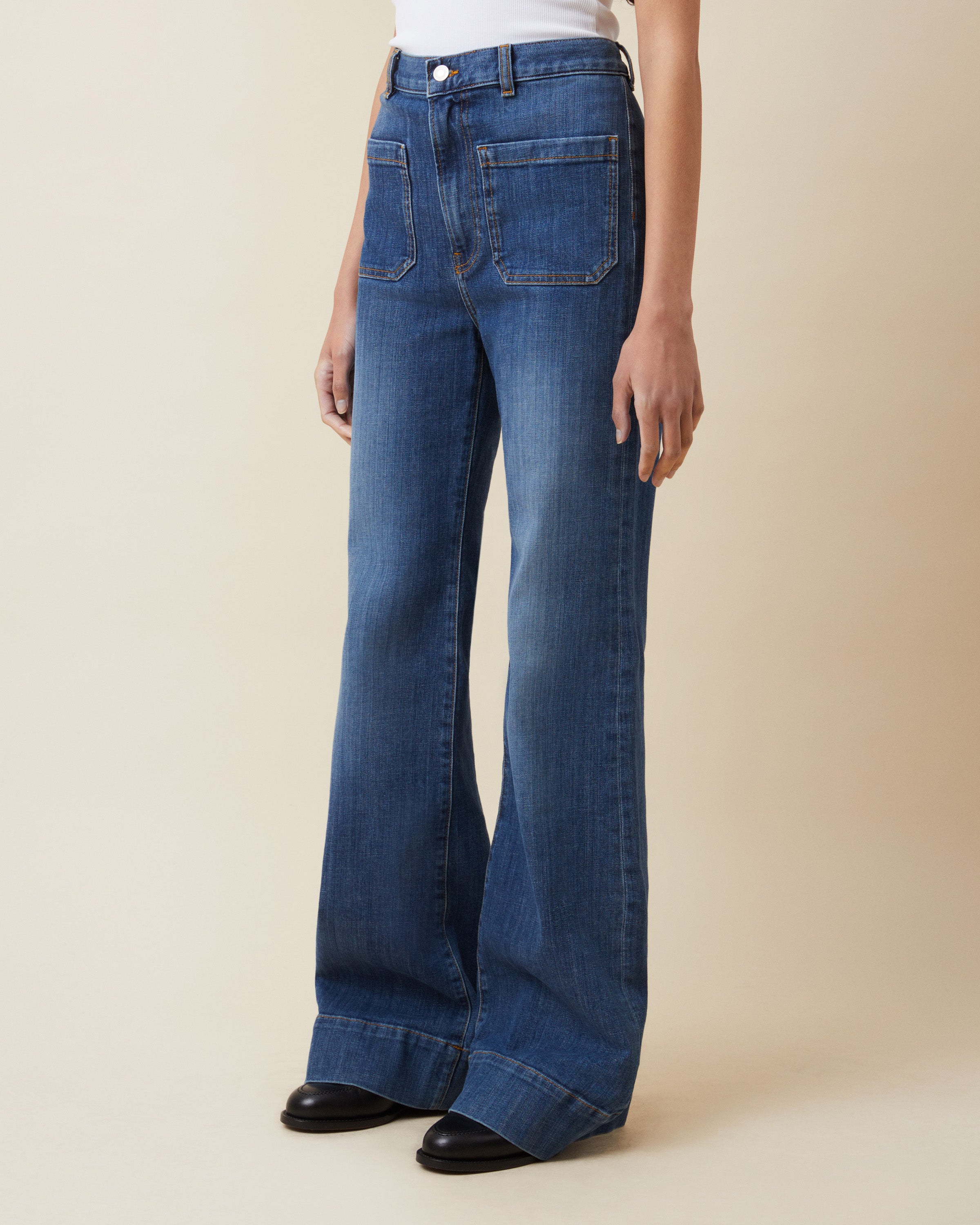 Person wearing blue flared jeans on a beige background