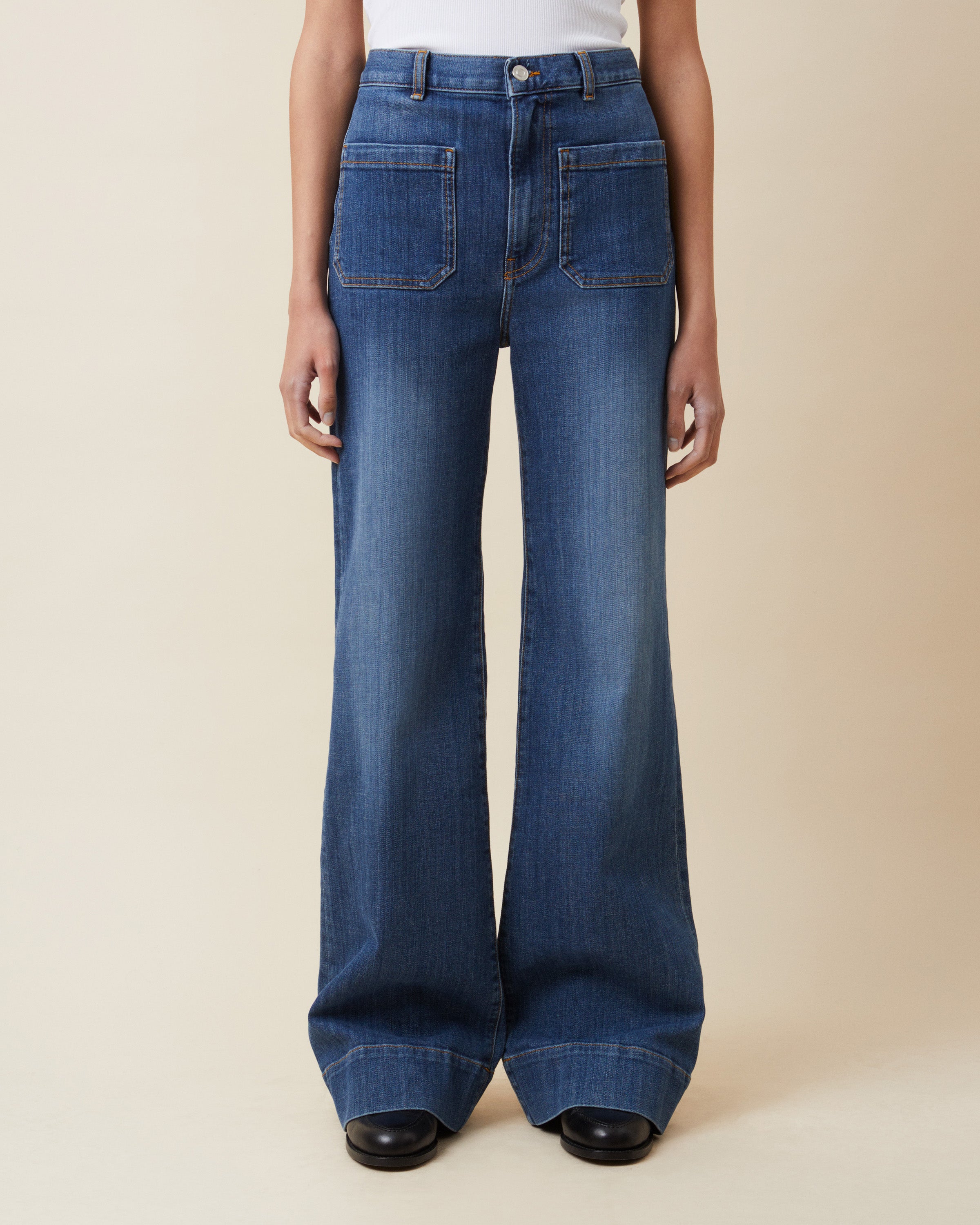 Person wearing blue flared jeans on a beige background