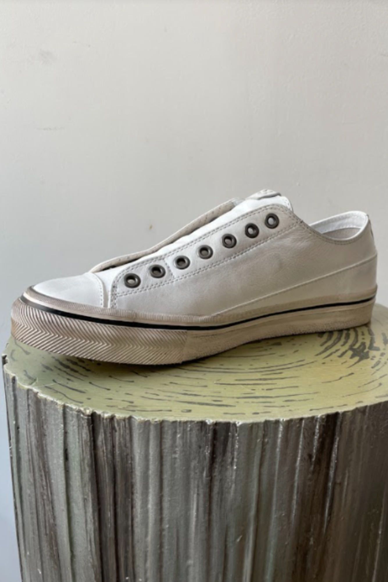 Beige, white sneaker on a cylindrical wooden block with a plain background