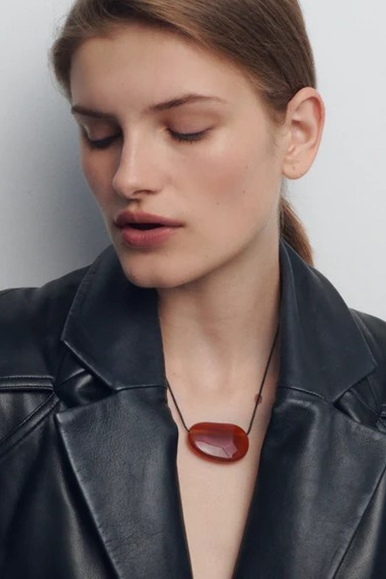 Woman wearing a black leather jacket with a red pendant necklace against a neutral background