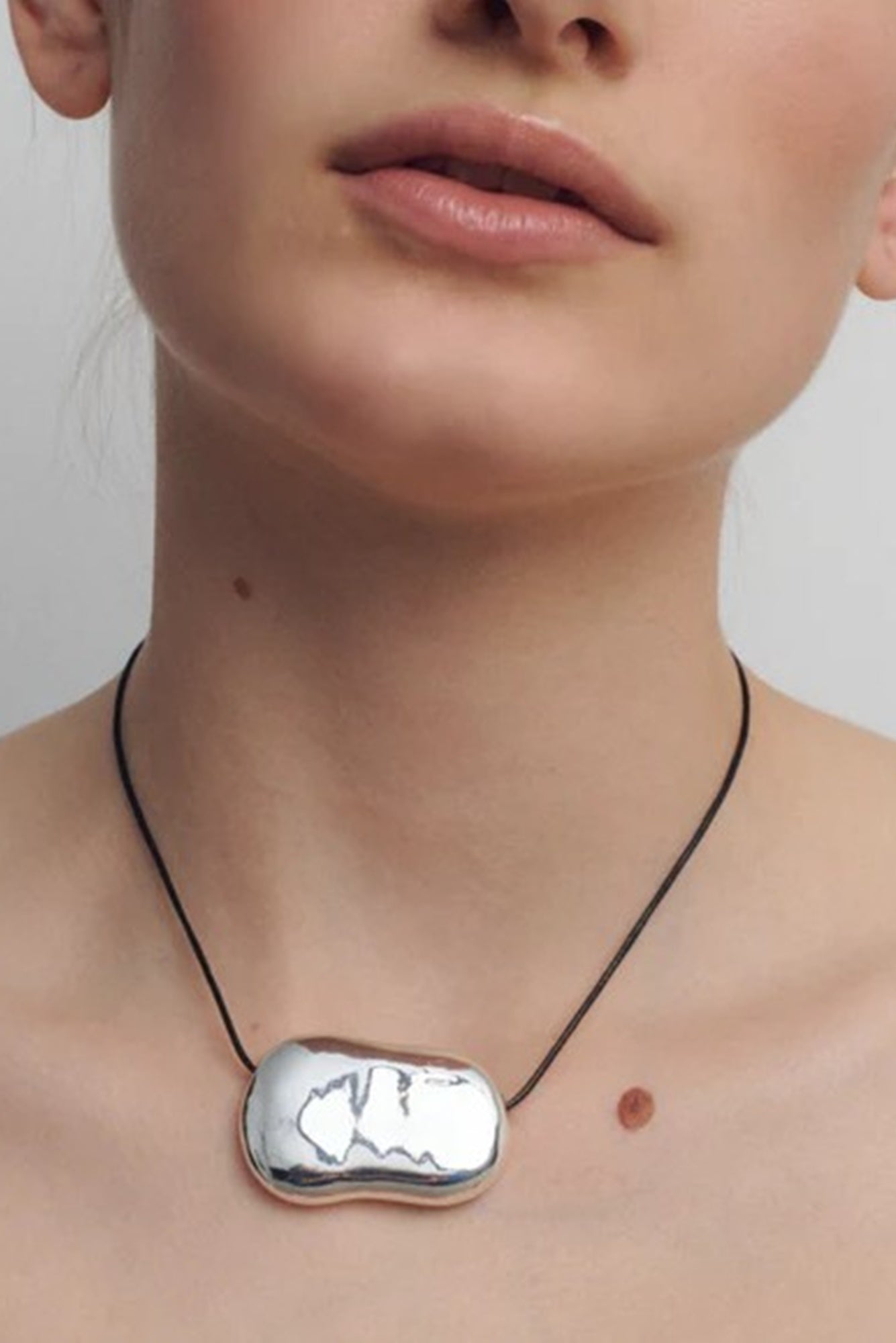 Close-up of a person wearing a silver necklace with a unique pendant on a plain background
