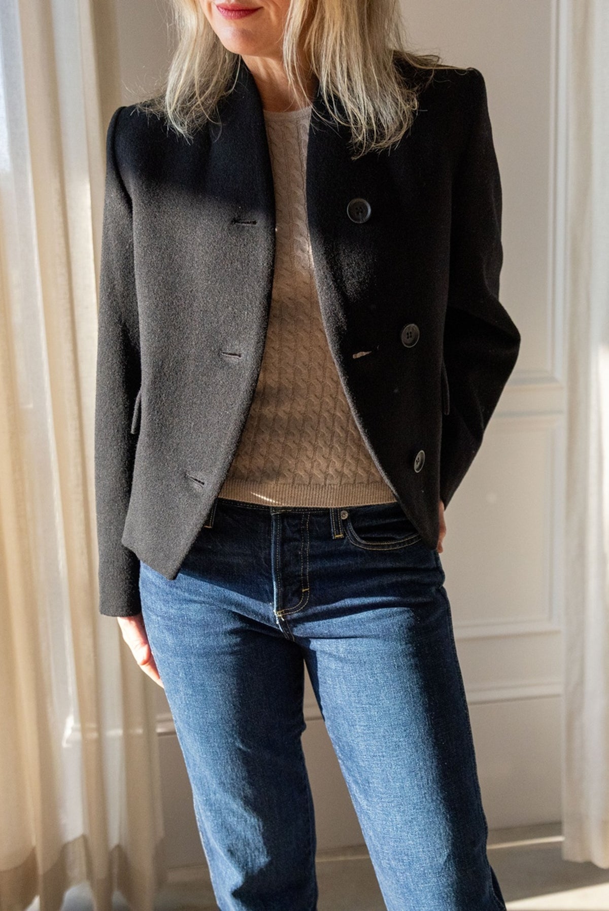 Close-up of the Lisa Yang Iora cable-knit top in sand under the black Dagmar short curved jacket