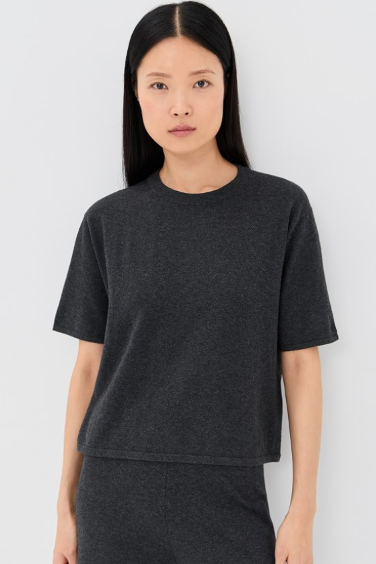 A woman modeling a dark charcoal gray short-sleeve crewneck knit top and matching dark gray pants against a light gray studio background.