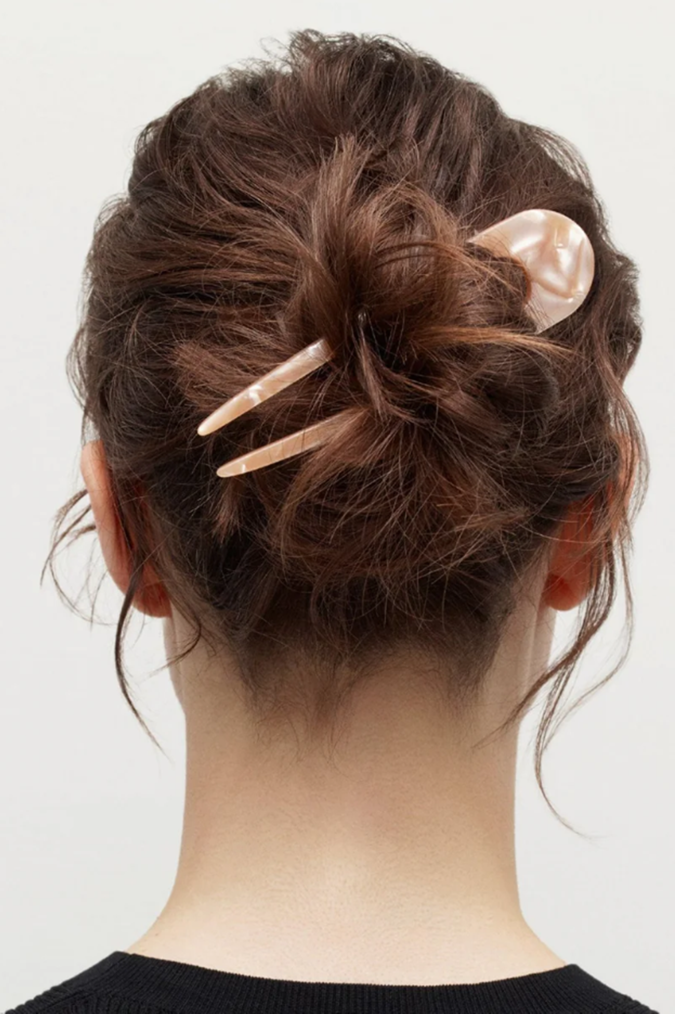 Back view of a person with styled hair featuring hairpins on a plain background