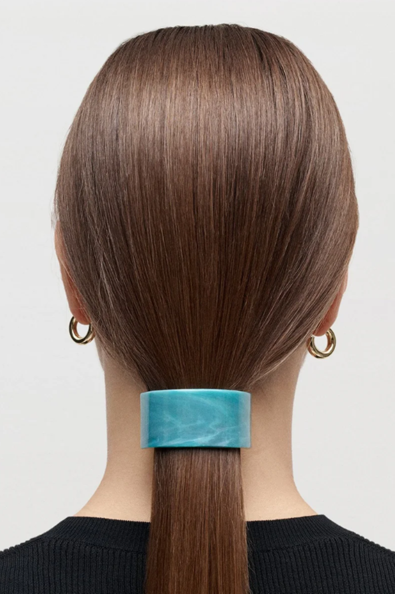 Person with brown hair tied in a ponytail using a blue frnch pony barrette against a white background