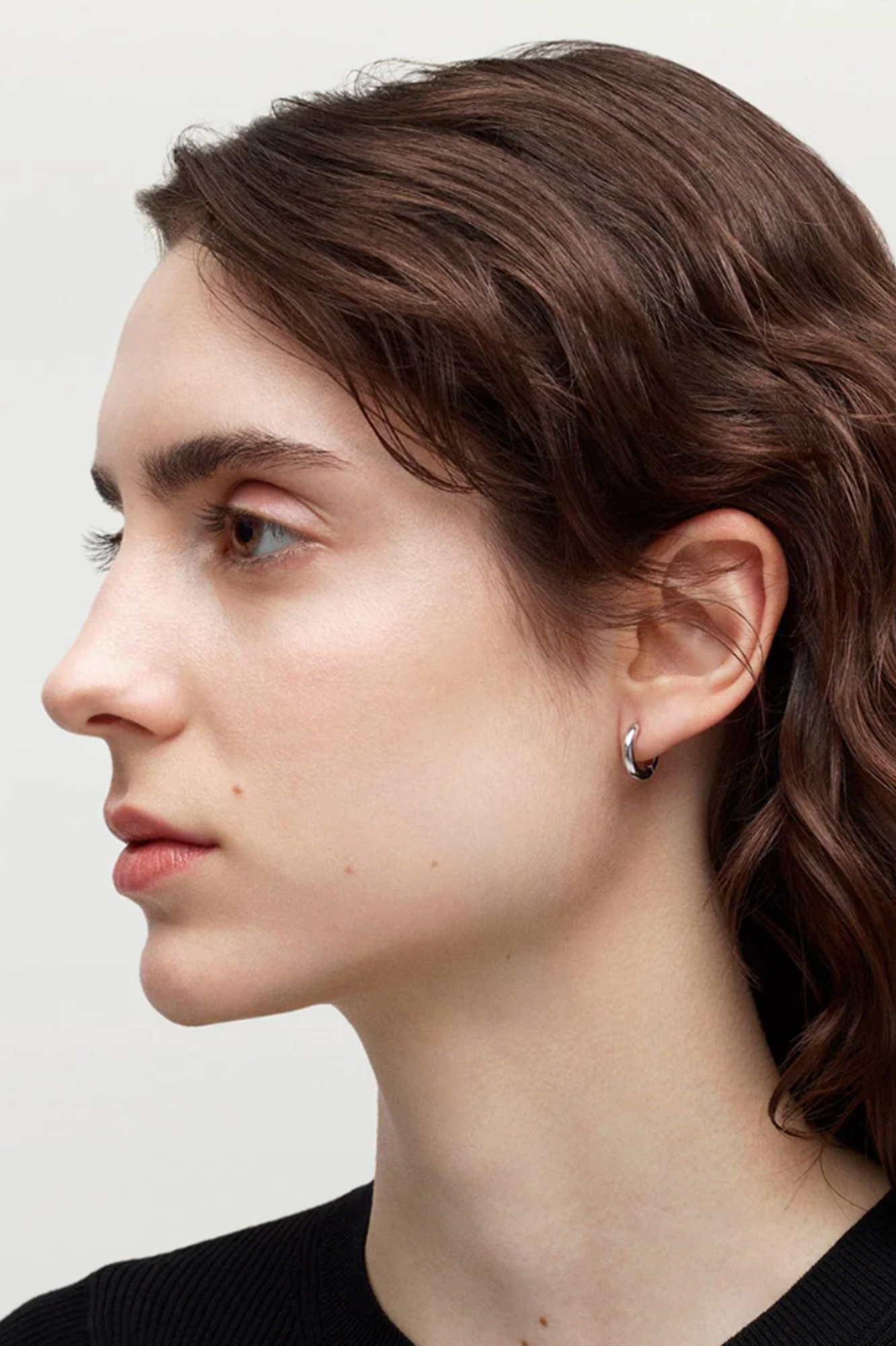 Close-up of a person wearing a small hoop earring on a plain background