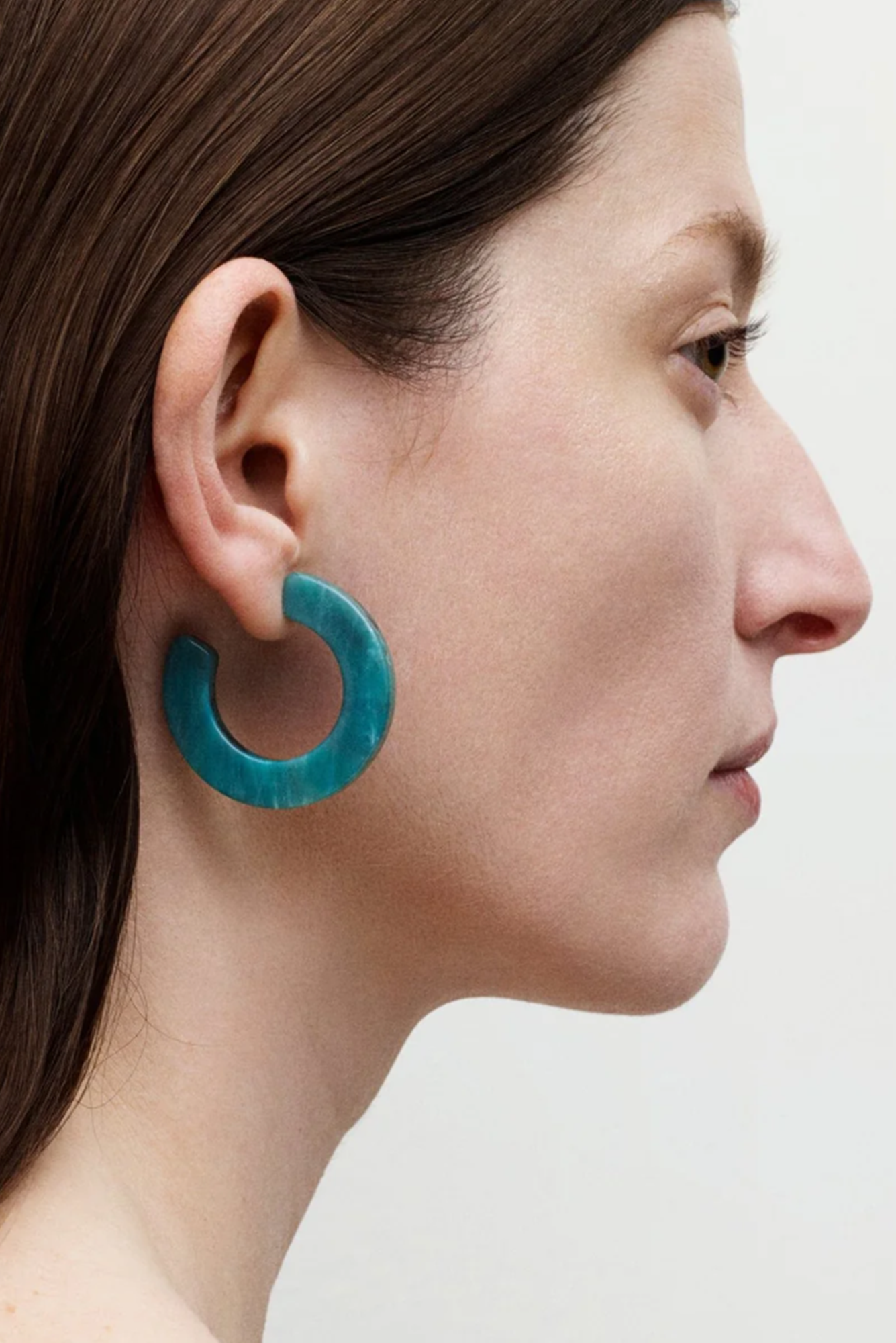 Close-up of a person wearing turquoise hoop earrings on a plain background