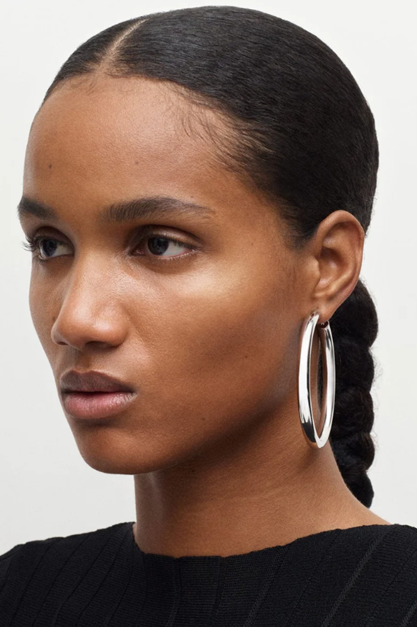 Woman with braided hair wearing a silver hoop earring on a plain background