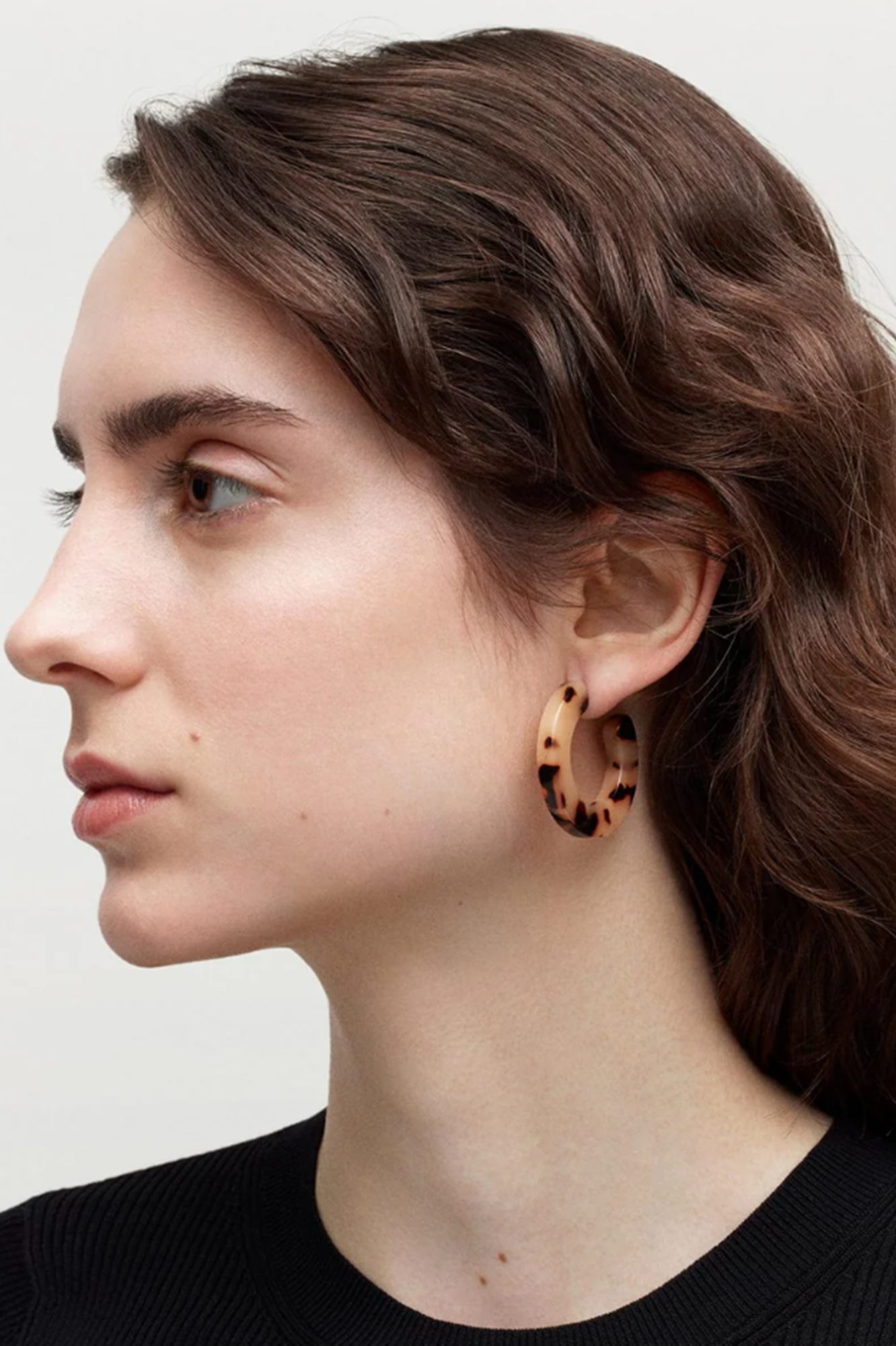 Person wearing leopard print hoop earrings with a neutral background